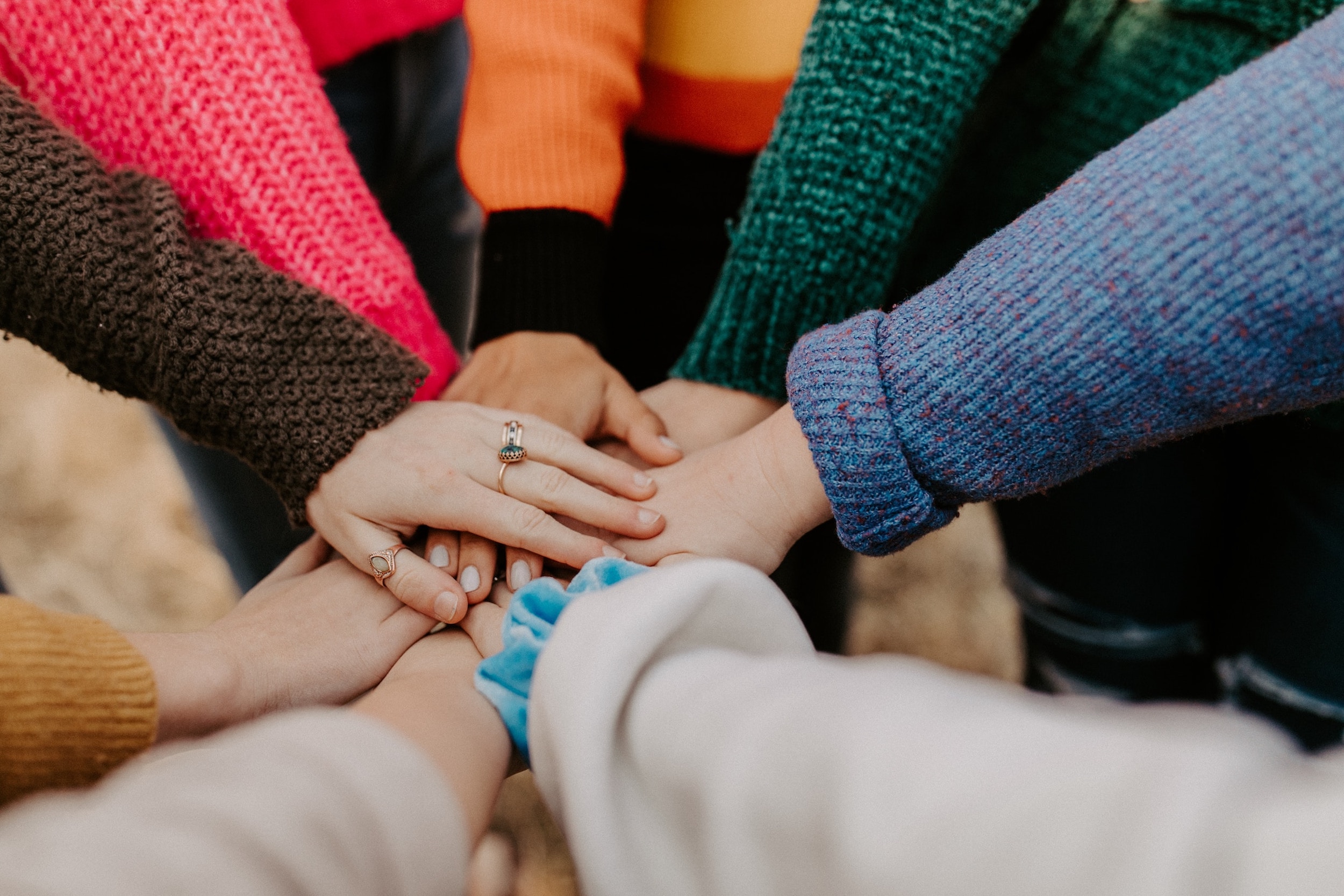 A group of people in colorful clothing place their hands together.