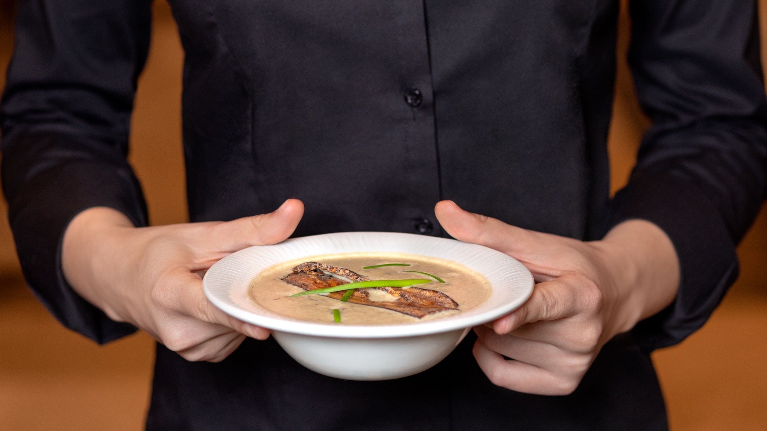 A man dressed in black holds a bowl of soup.