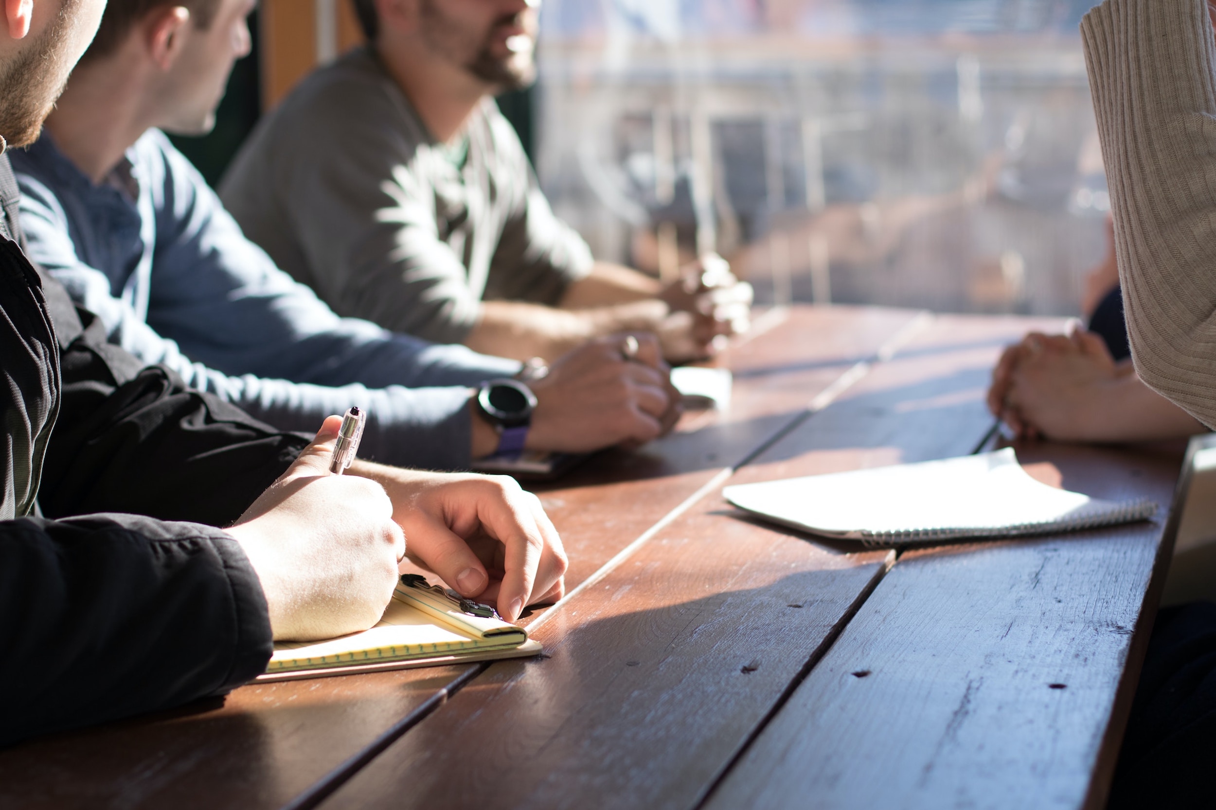 A group of men sit at a desk while being trained by an instructor.