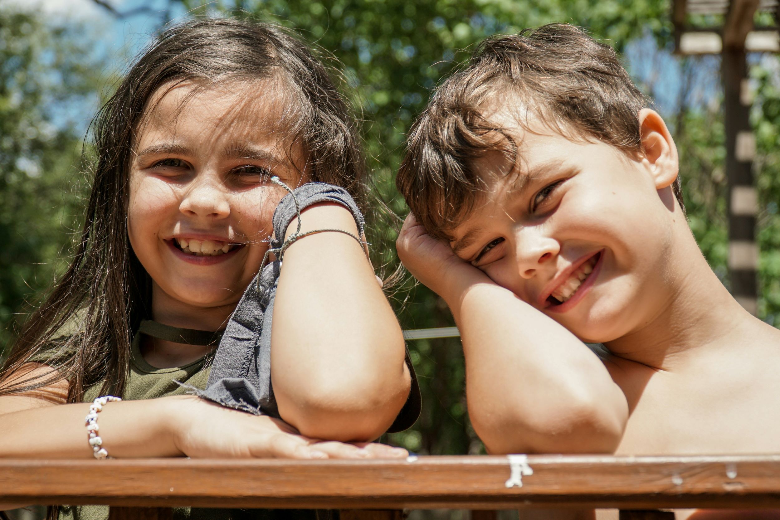 Two children smile in front of a cluster of trees.