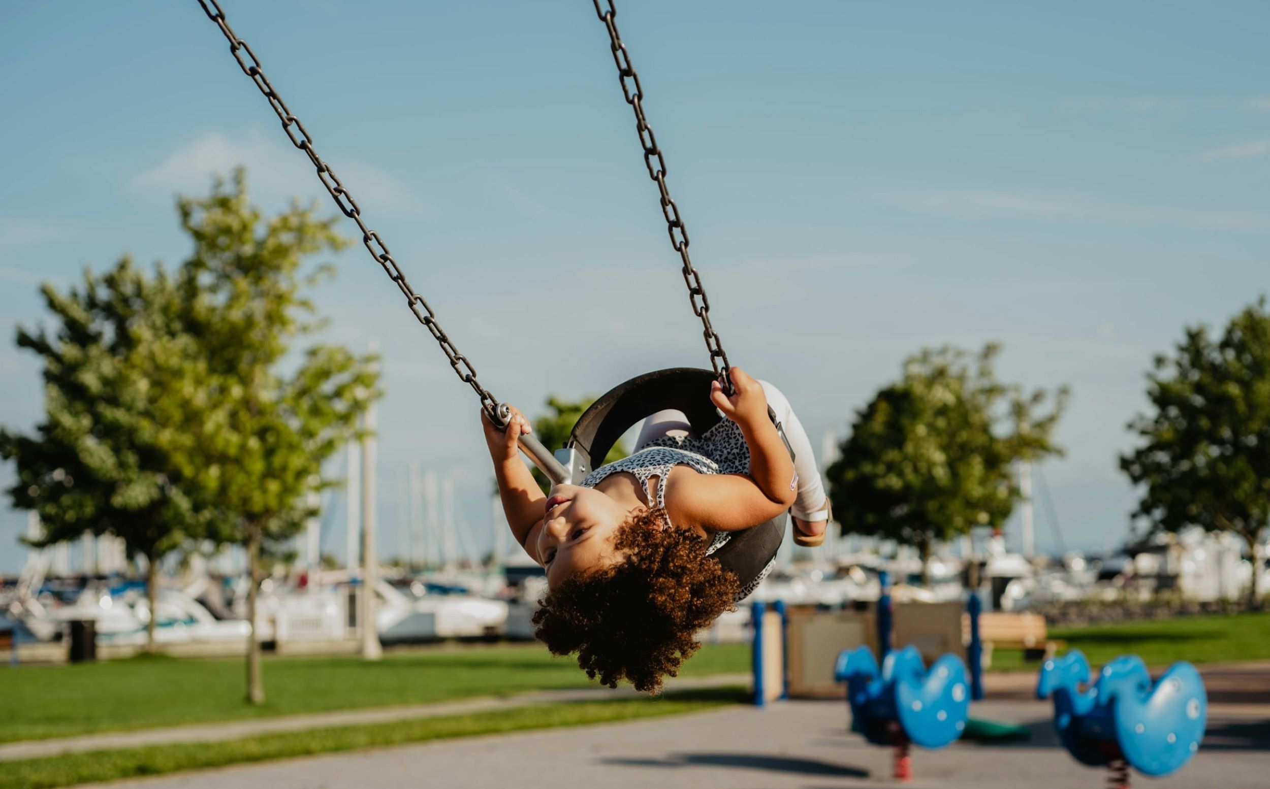 A child smiles while being pushed on a small swing.