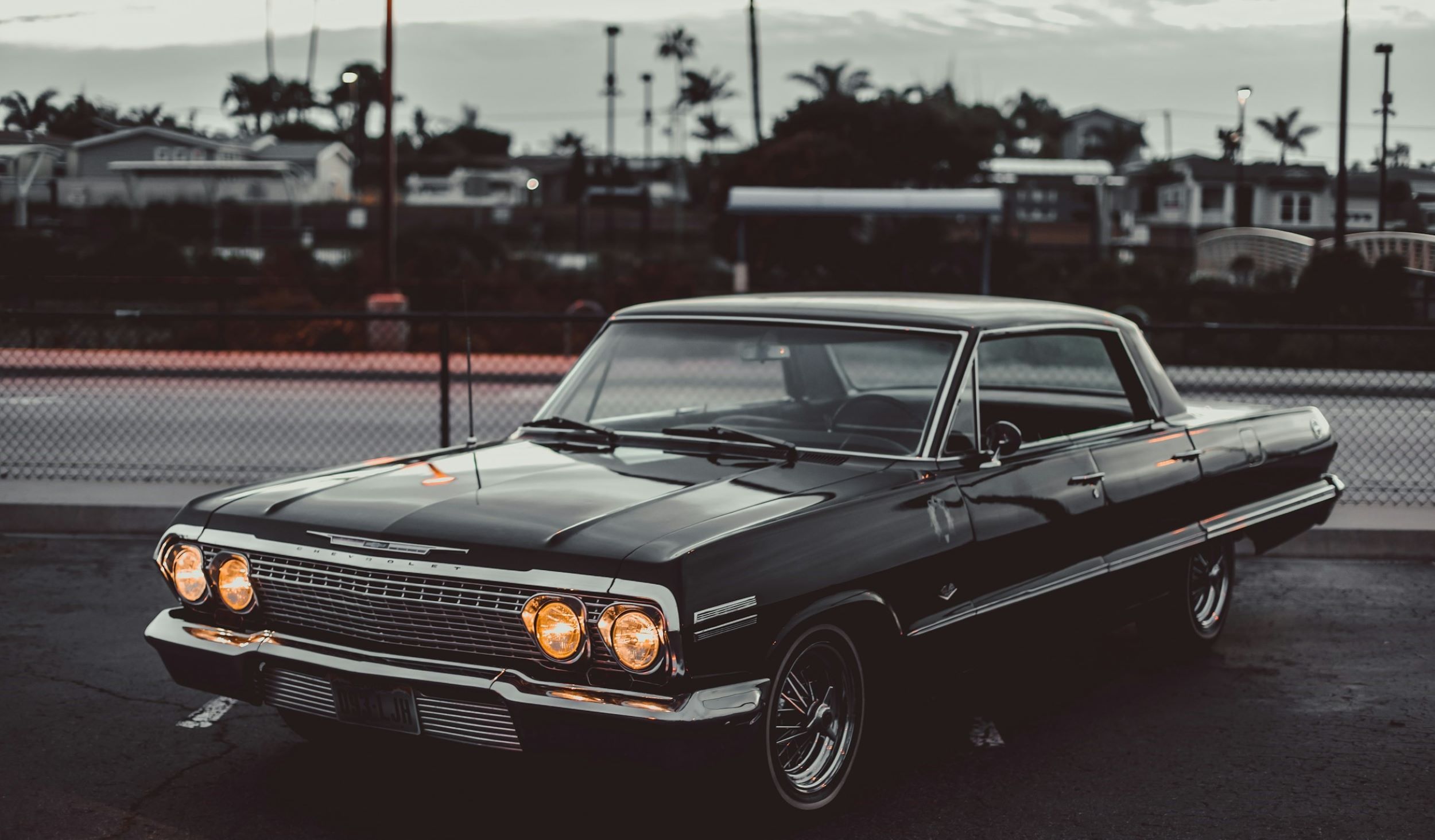 A black car is parked in front of a narrow road. 