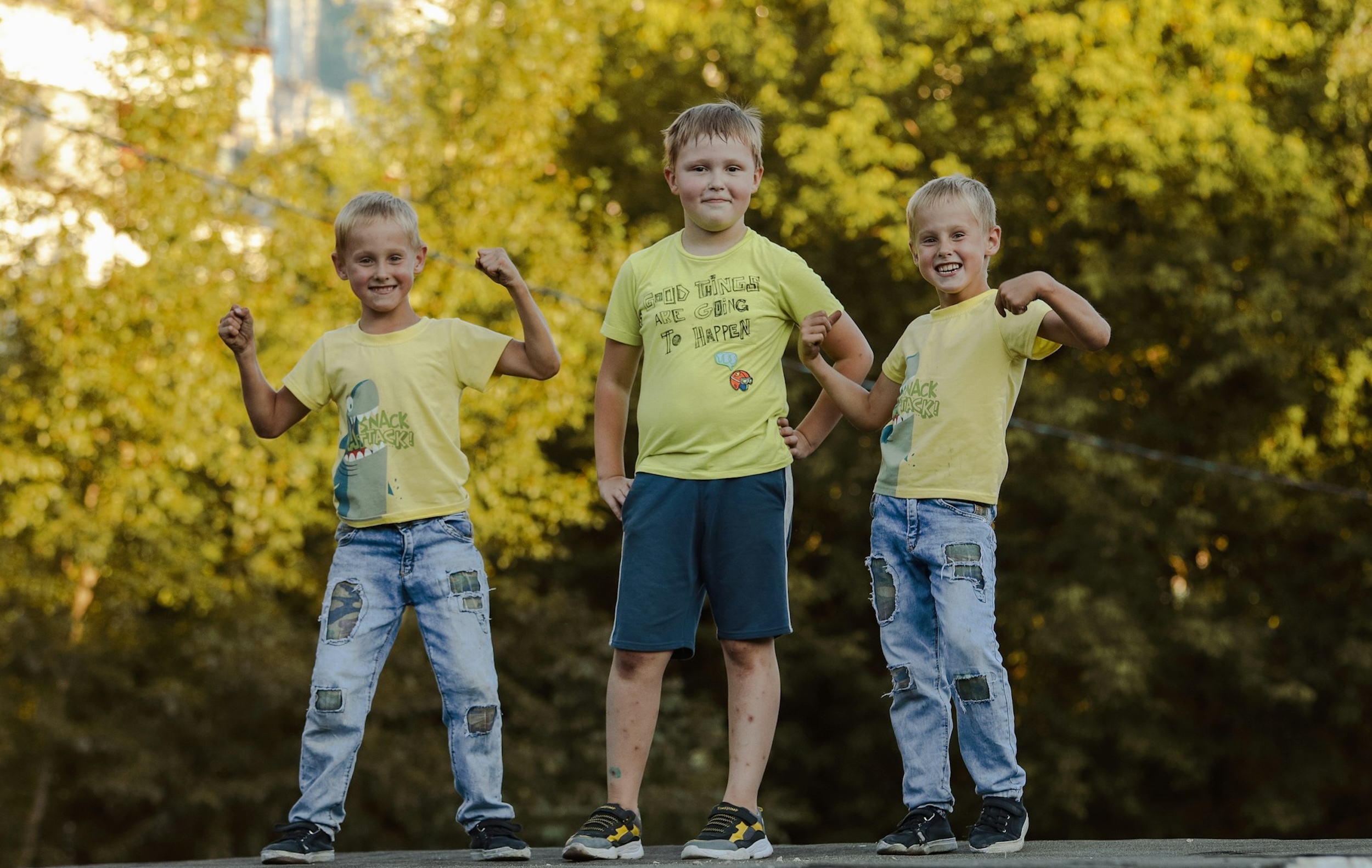 Three boys smile and pose in front of trees with bright colored leaves.