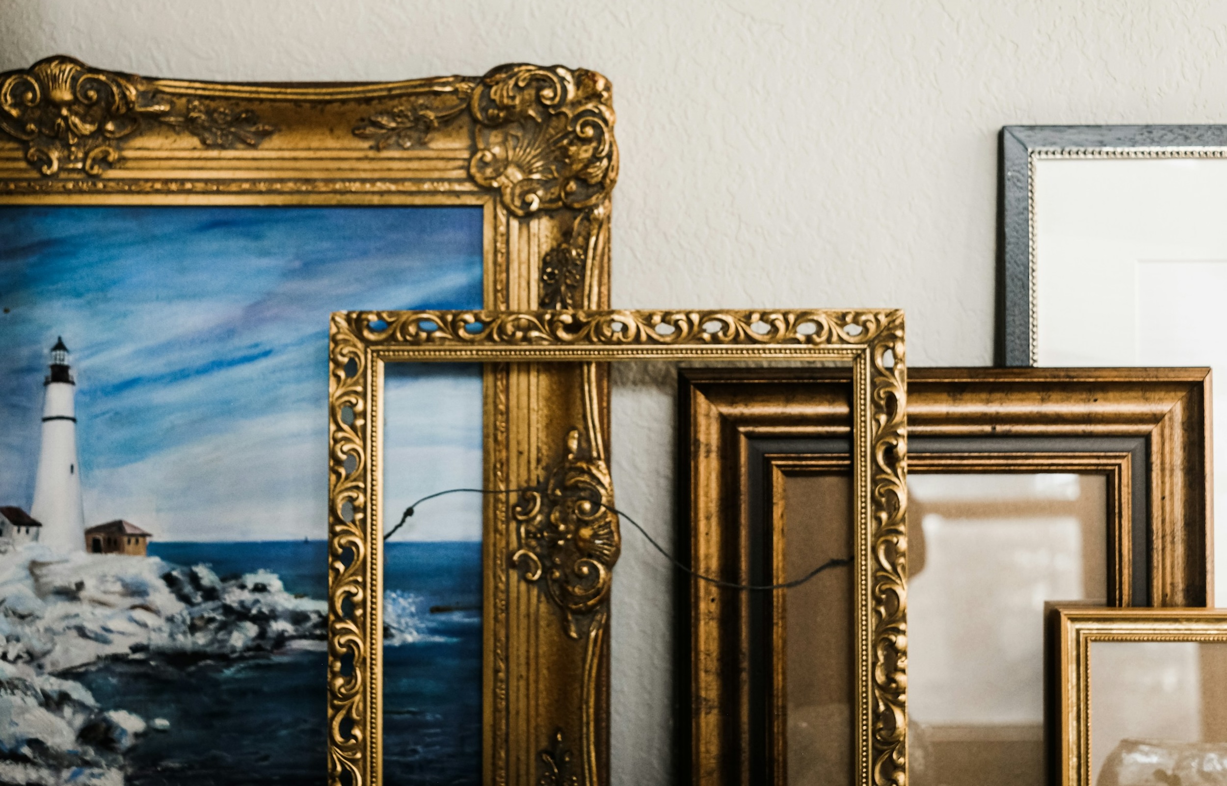 A colorful painting of a lighthouse is surrounded by gold frames of different sizes.