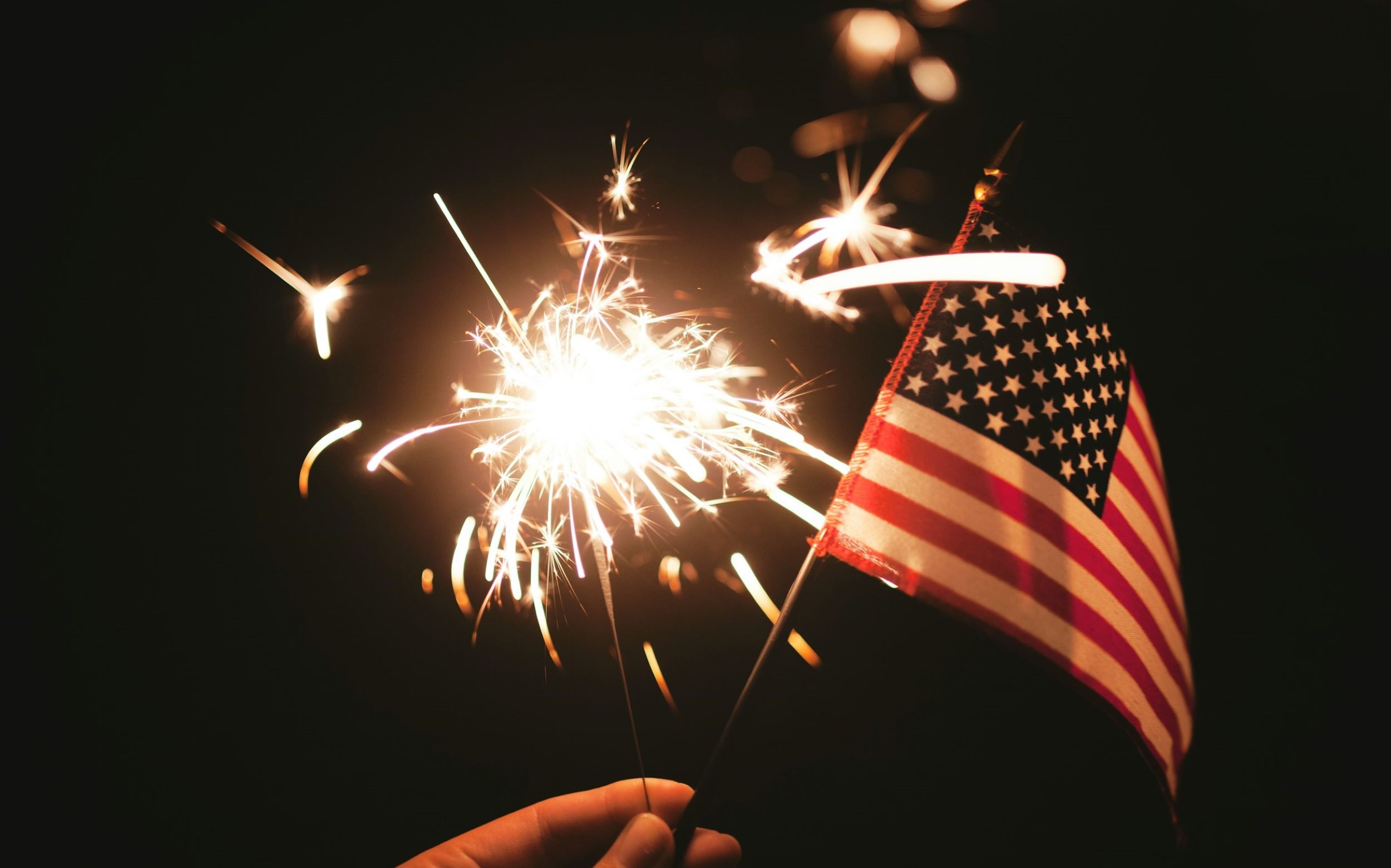A person holds a small firecracker and the American flag.