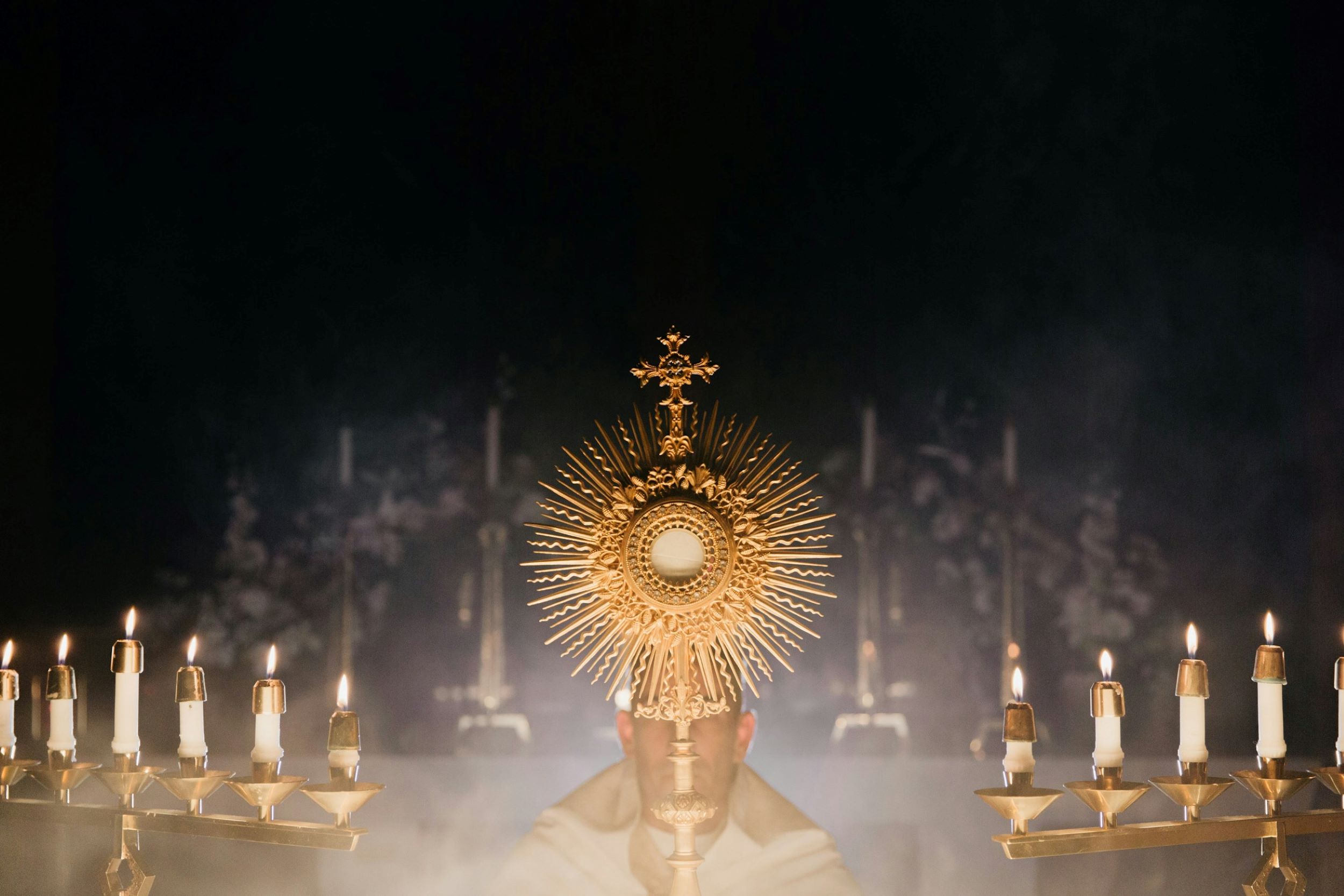 A priest kneels in front of an altar with a cross and candles.
