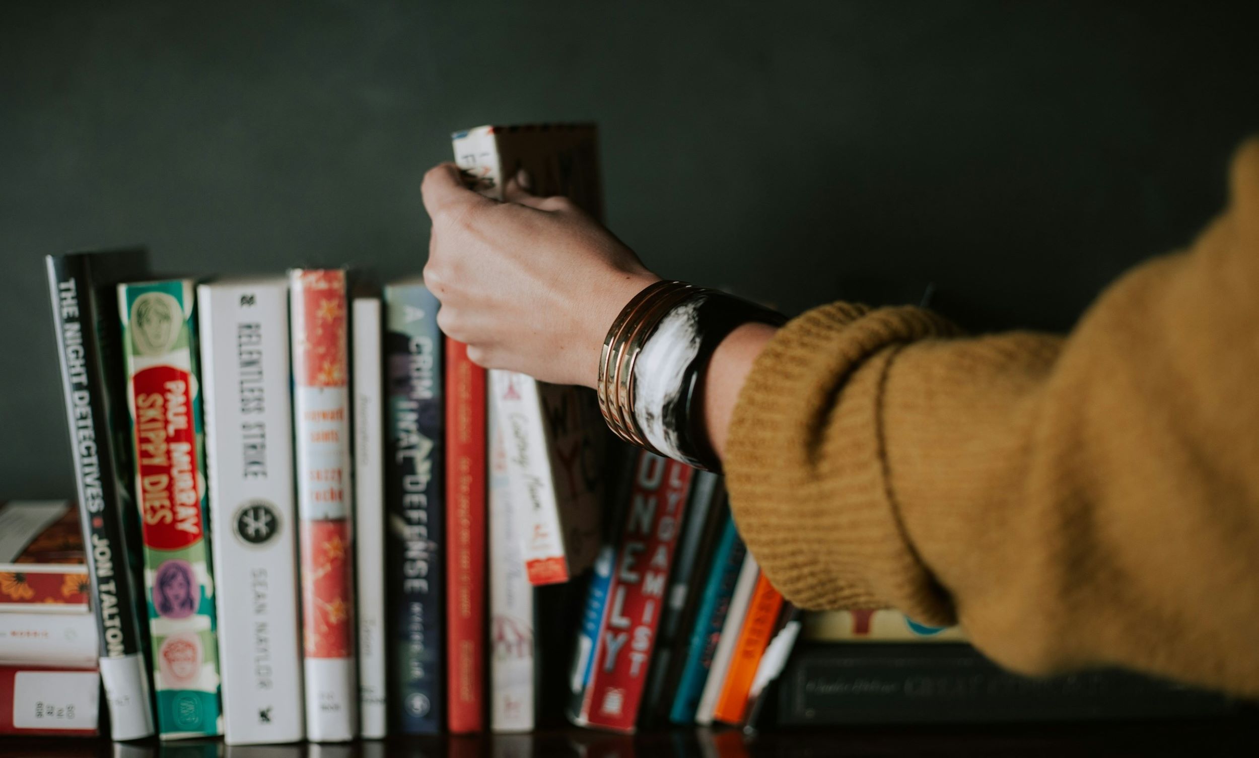 A woman clutches a book that was taken from a small shelf.