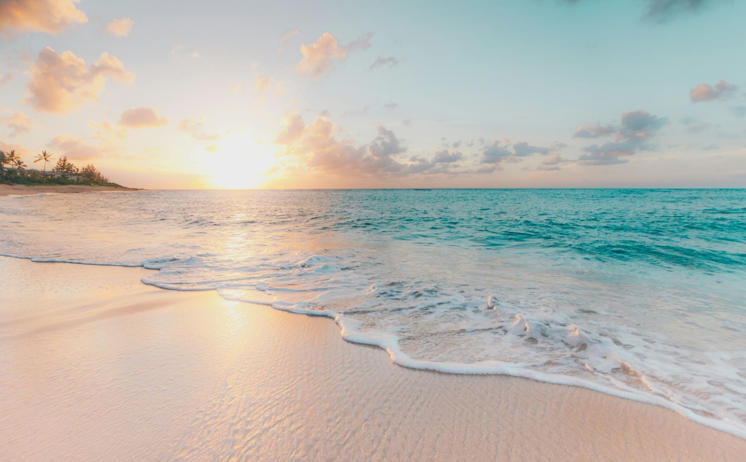 The sun rises over a beach with clear blue water.