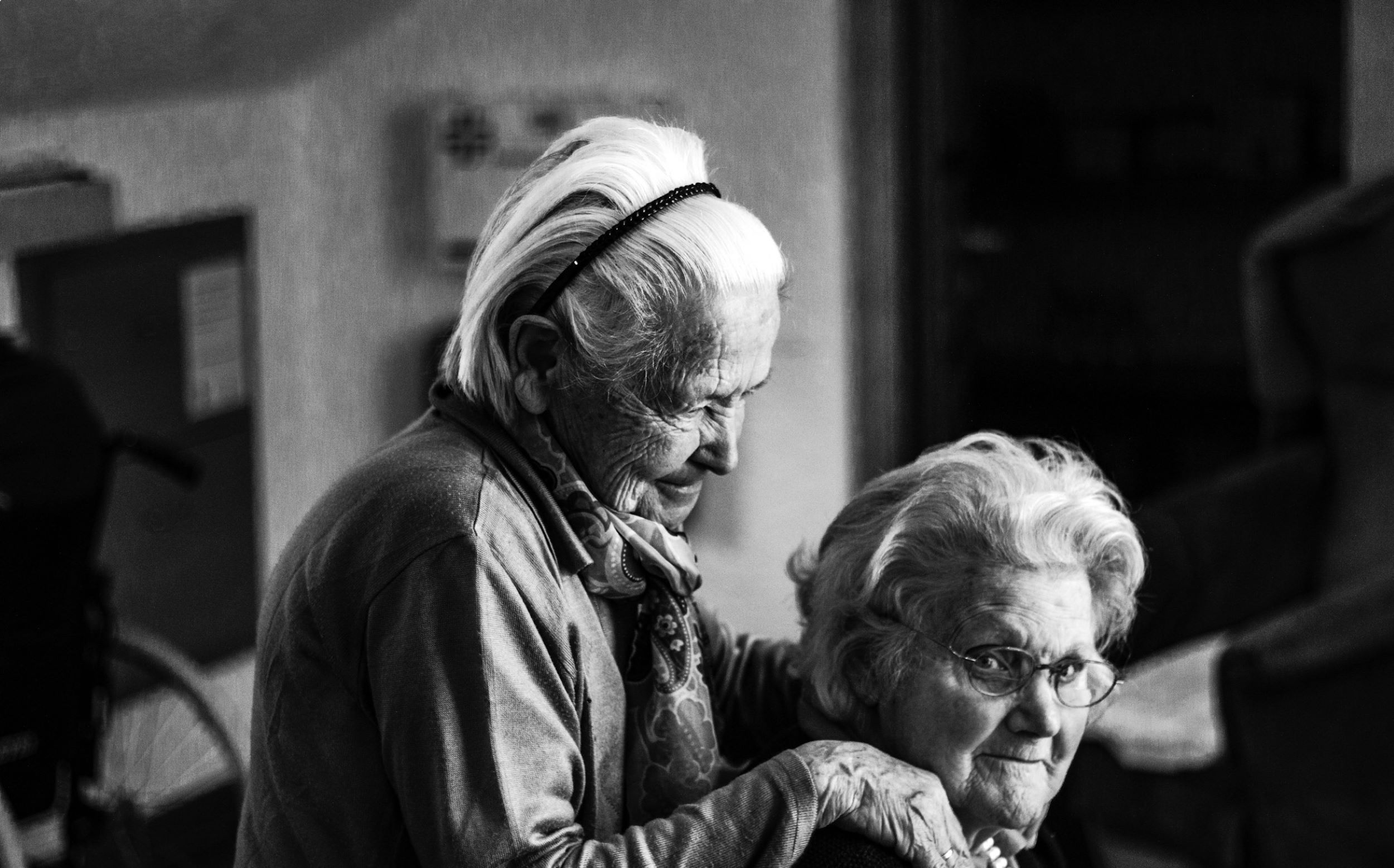 A black and white photo of two elderly women in front of a blurred background.