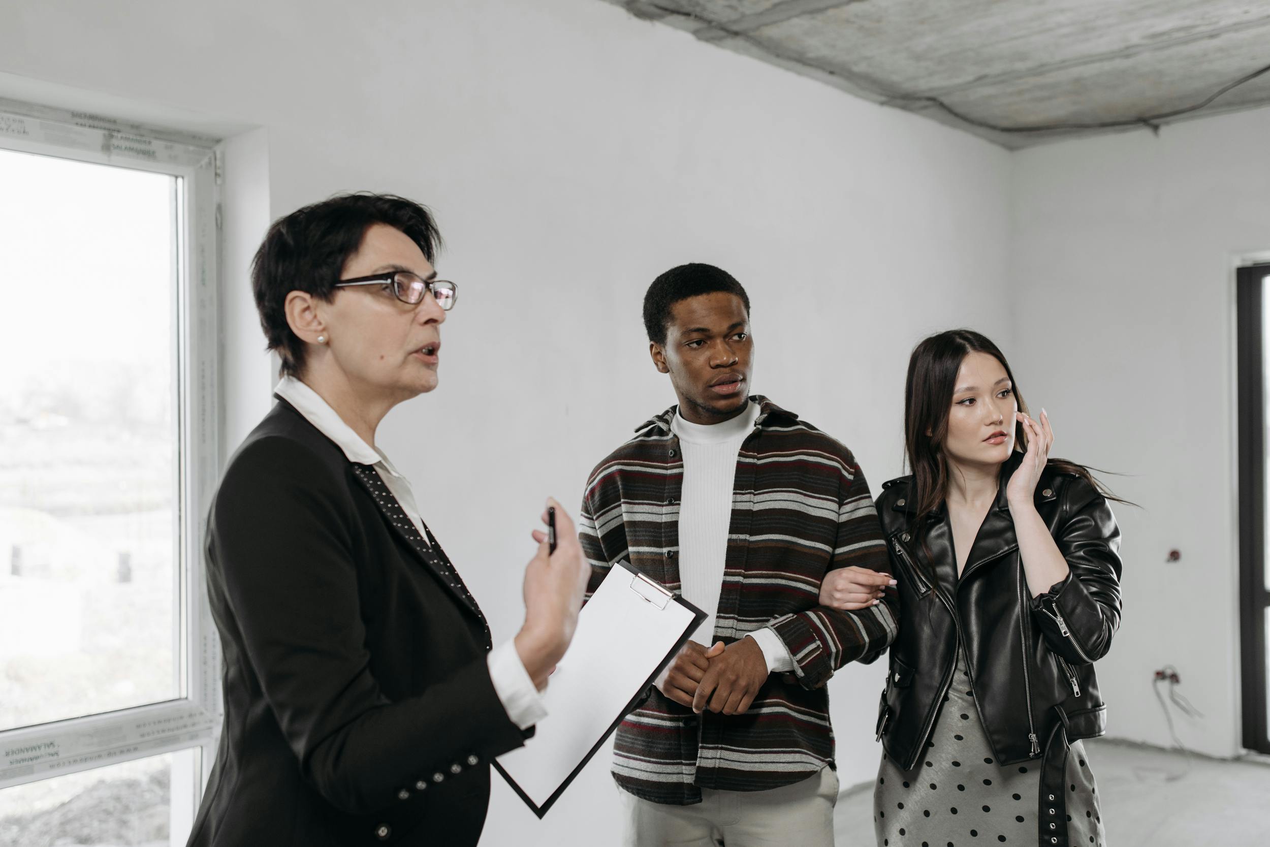 An agent speaks with a couple in a room with oversized windows.