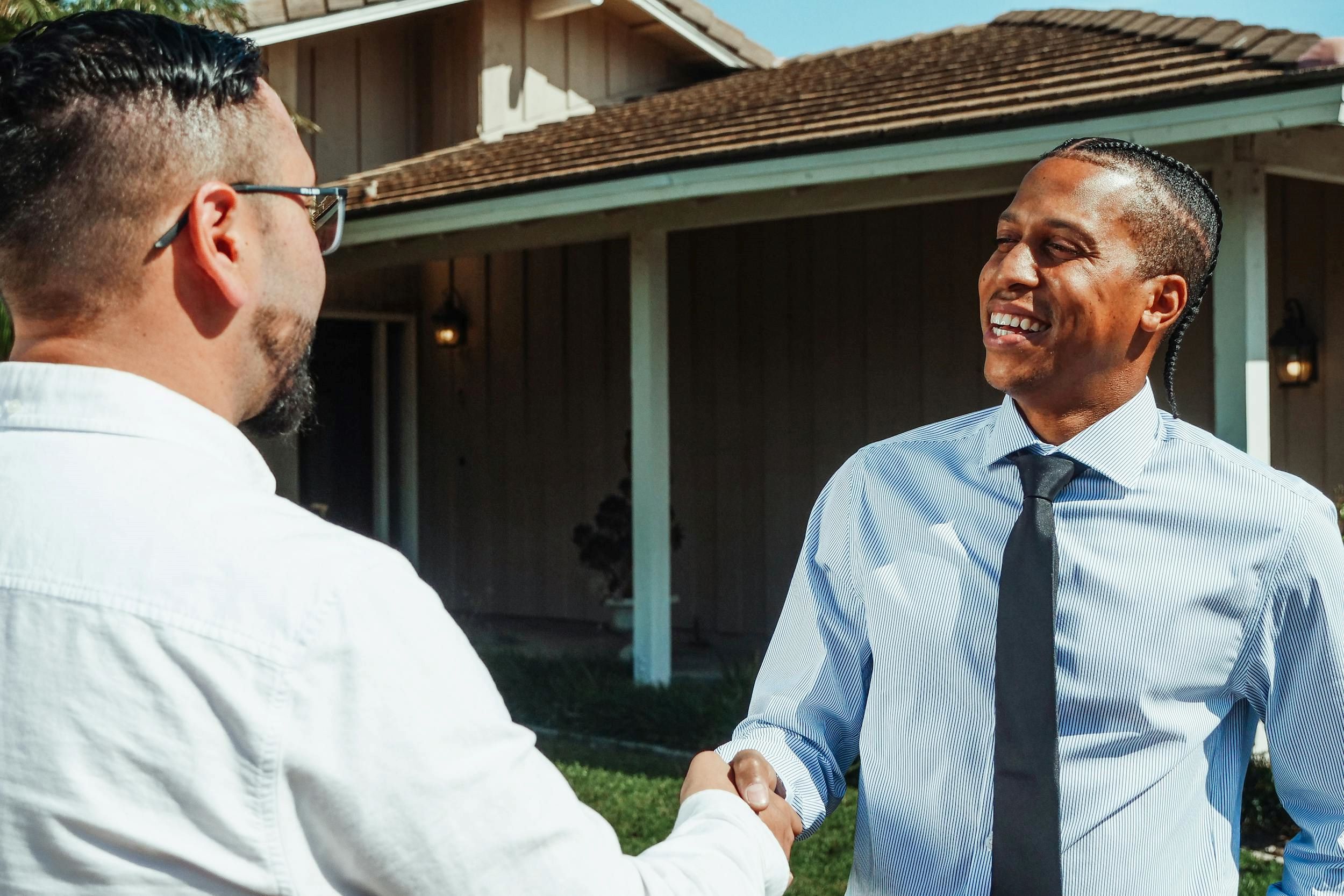An agent shakes hands with a man outside of a building.