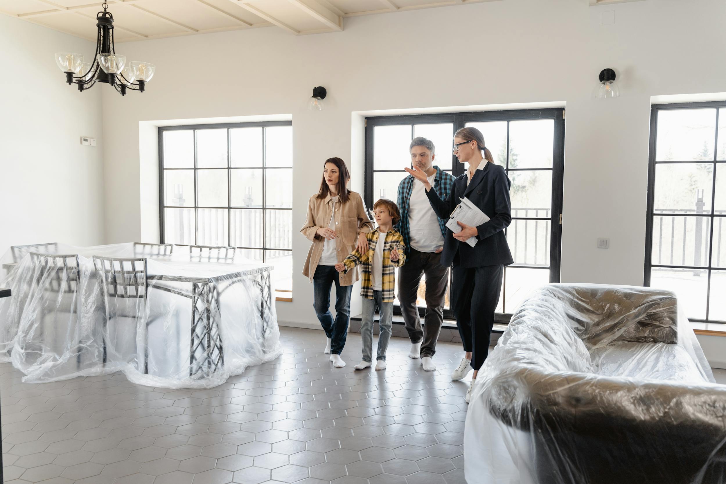 An agent and a family walks through a spacious home with furniture covered in plastic.
