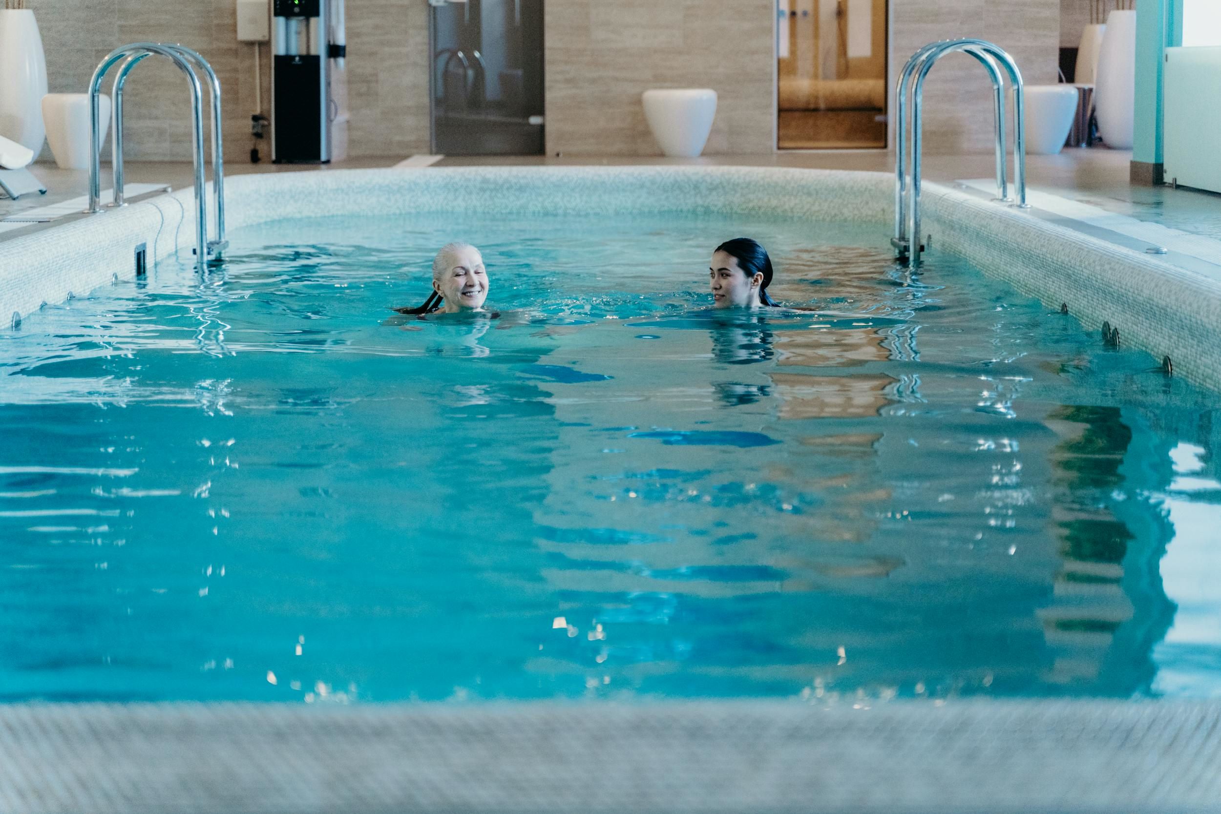 Two women smile while swimming in a pool.