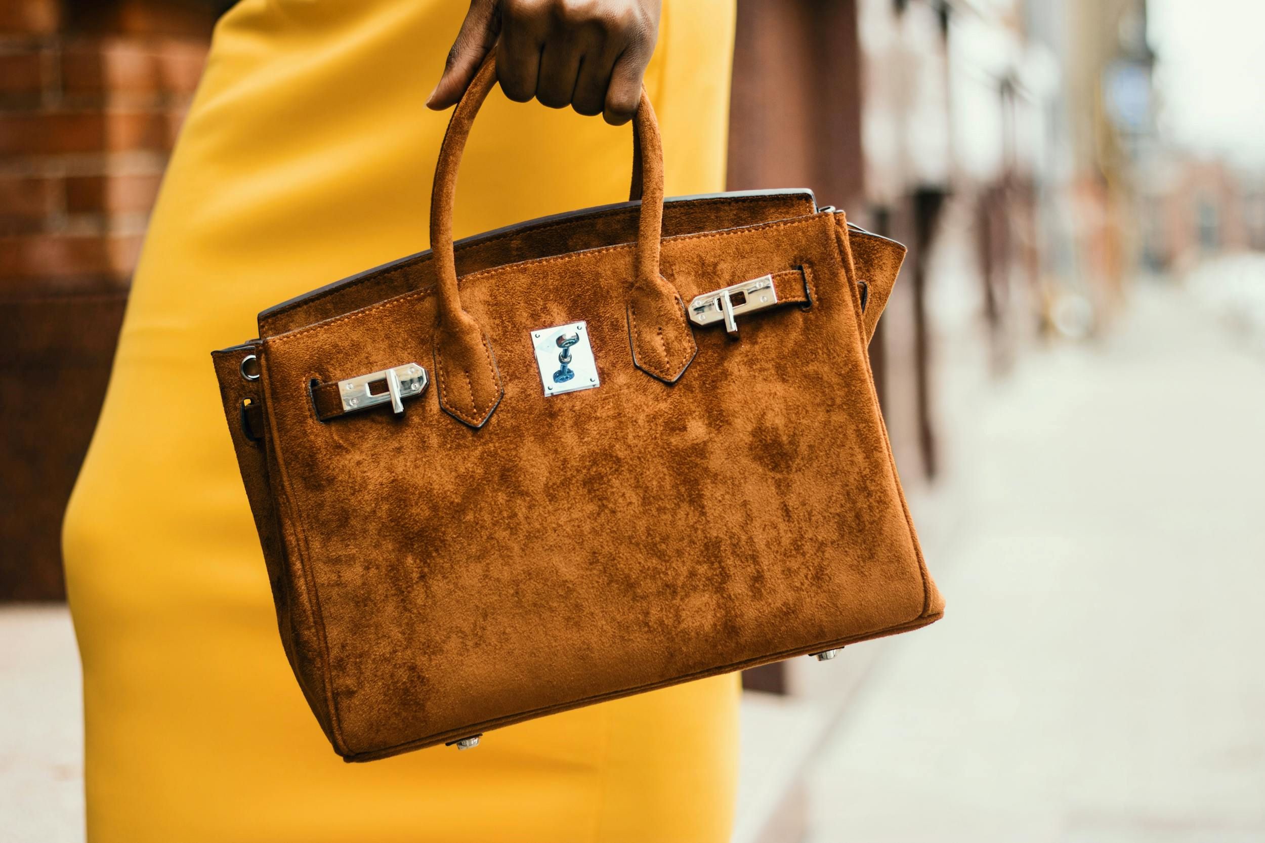A woman holds a brown bag near a retail store.