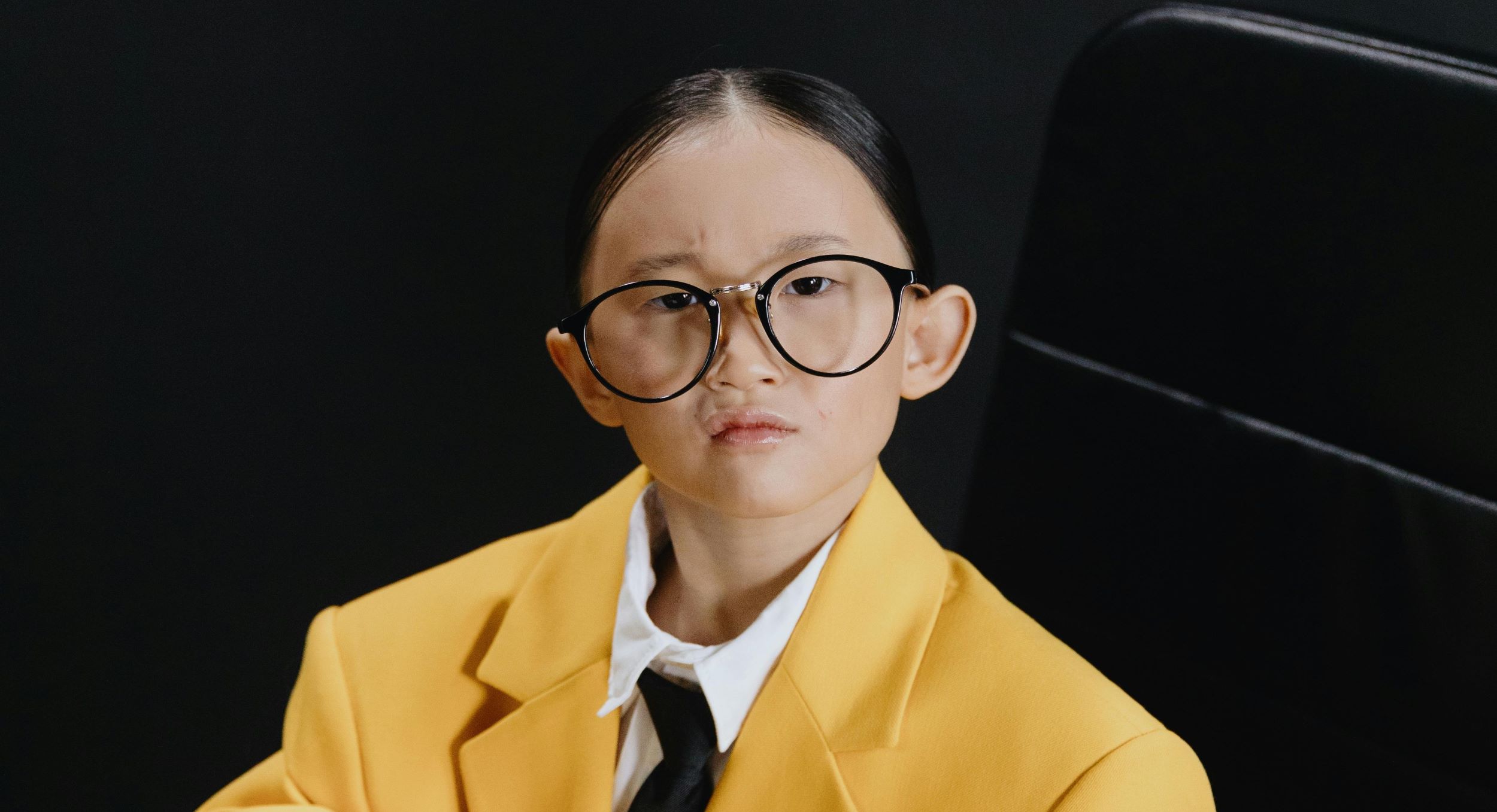 A young girl wears an oversized yellow blazer and poses for the camera.