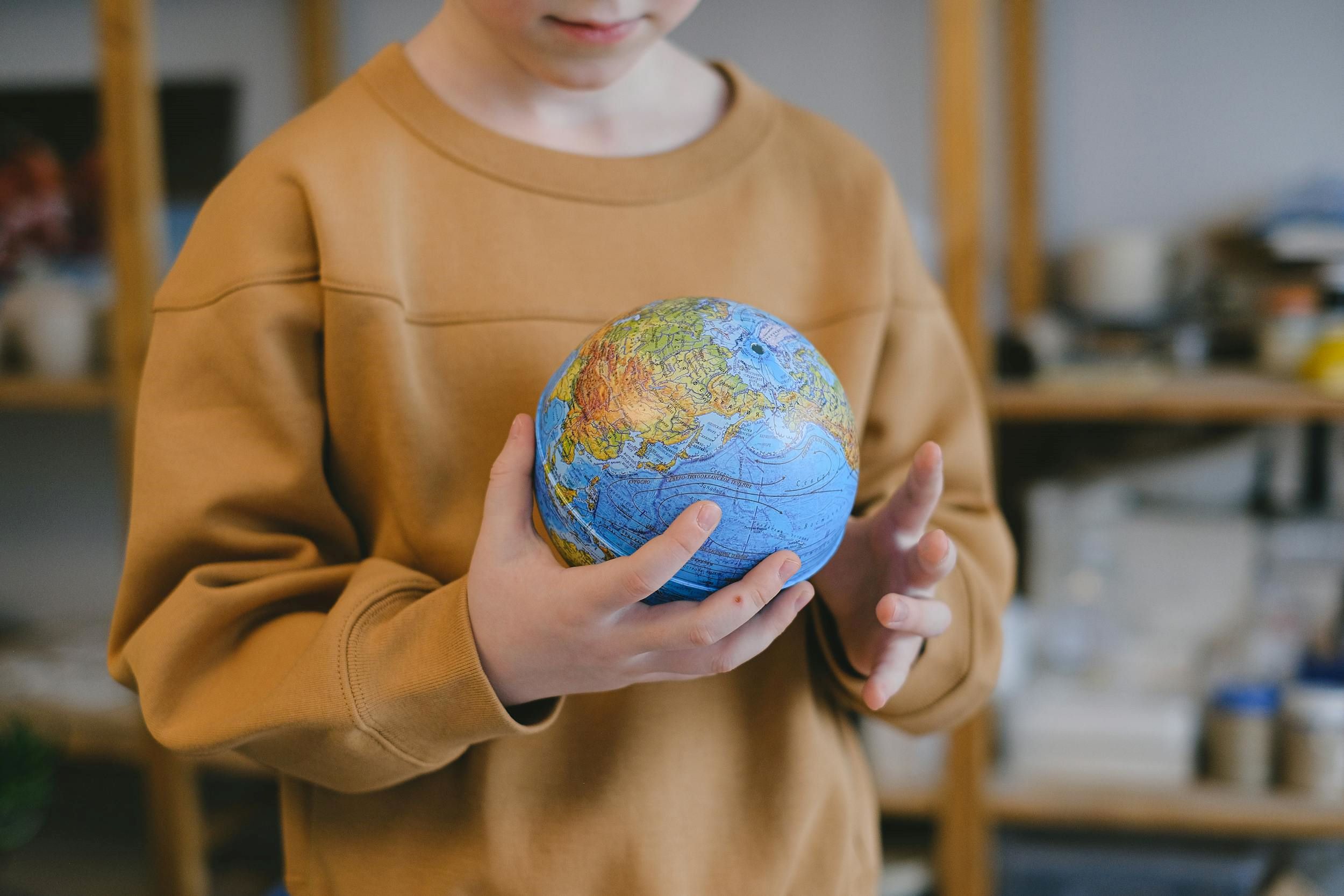A child smiles while carrying a small globe in his hands.