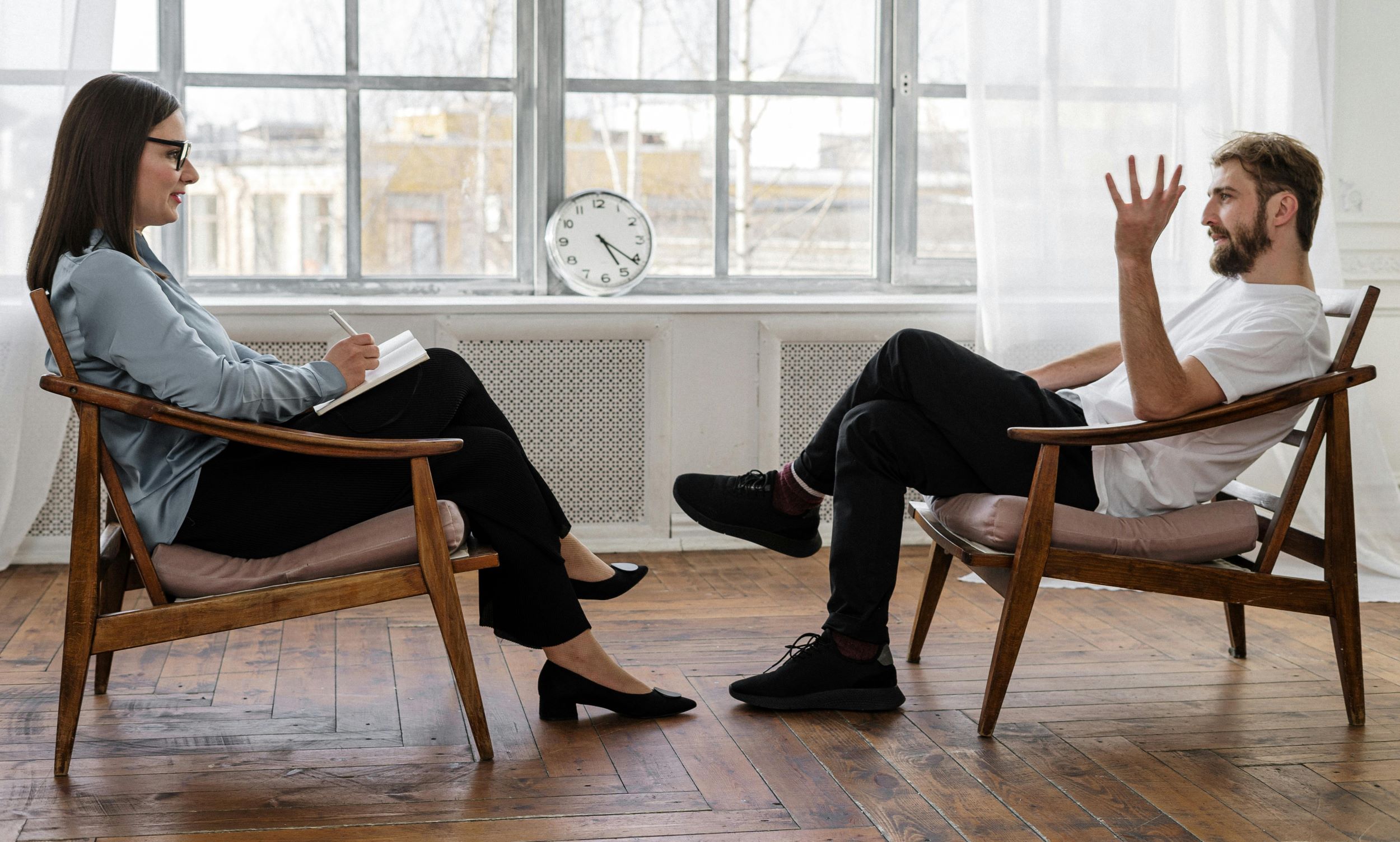 A counselor and patient have a session in a room with minimalist furniture. 