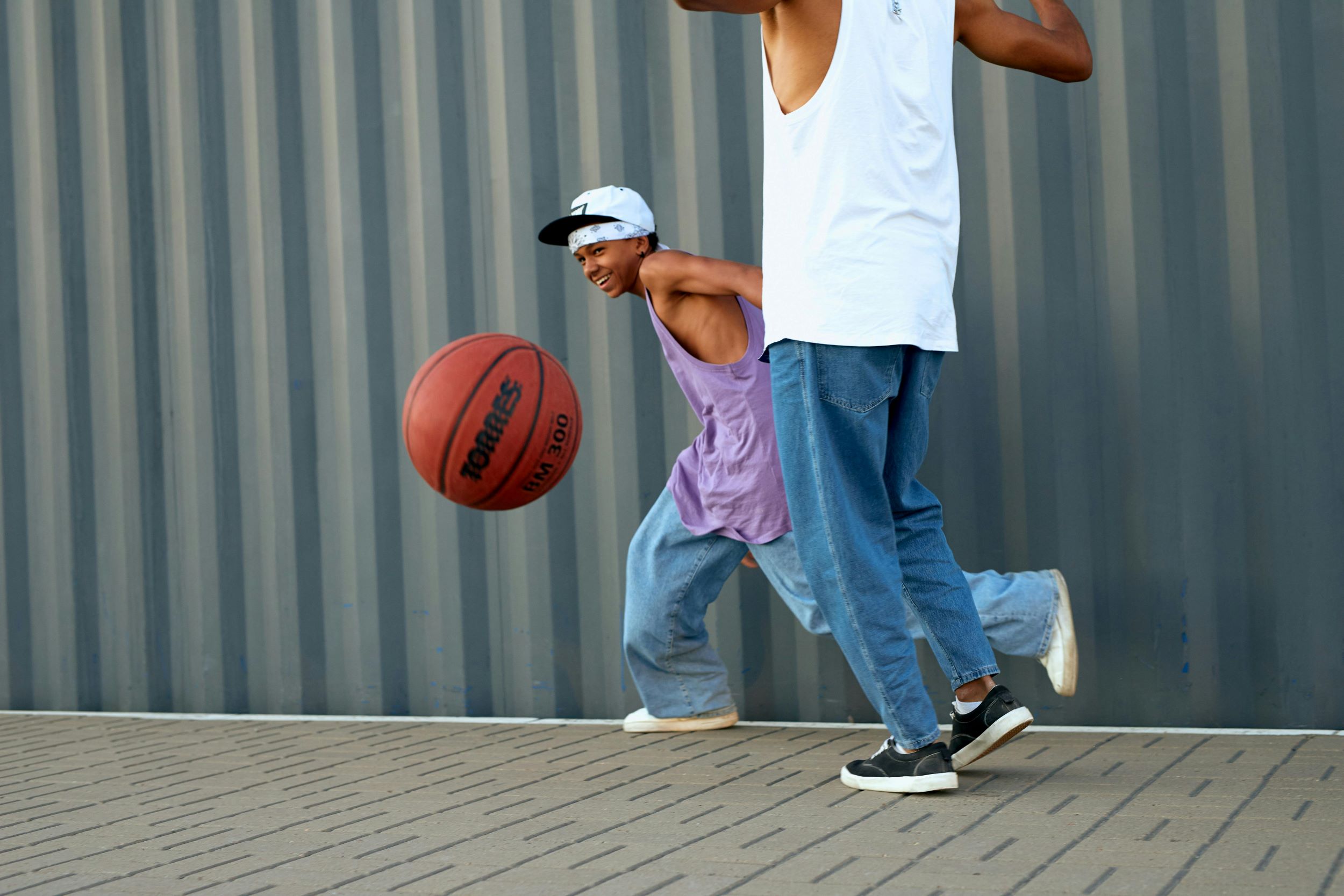 Two teens play basketball in front of a gray wall.