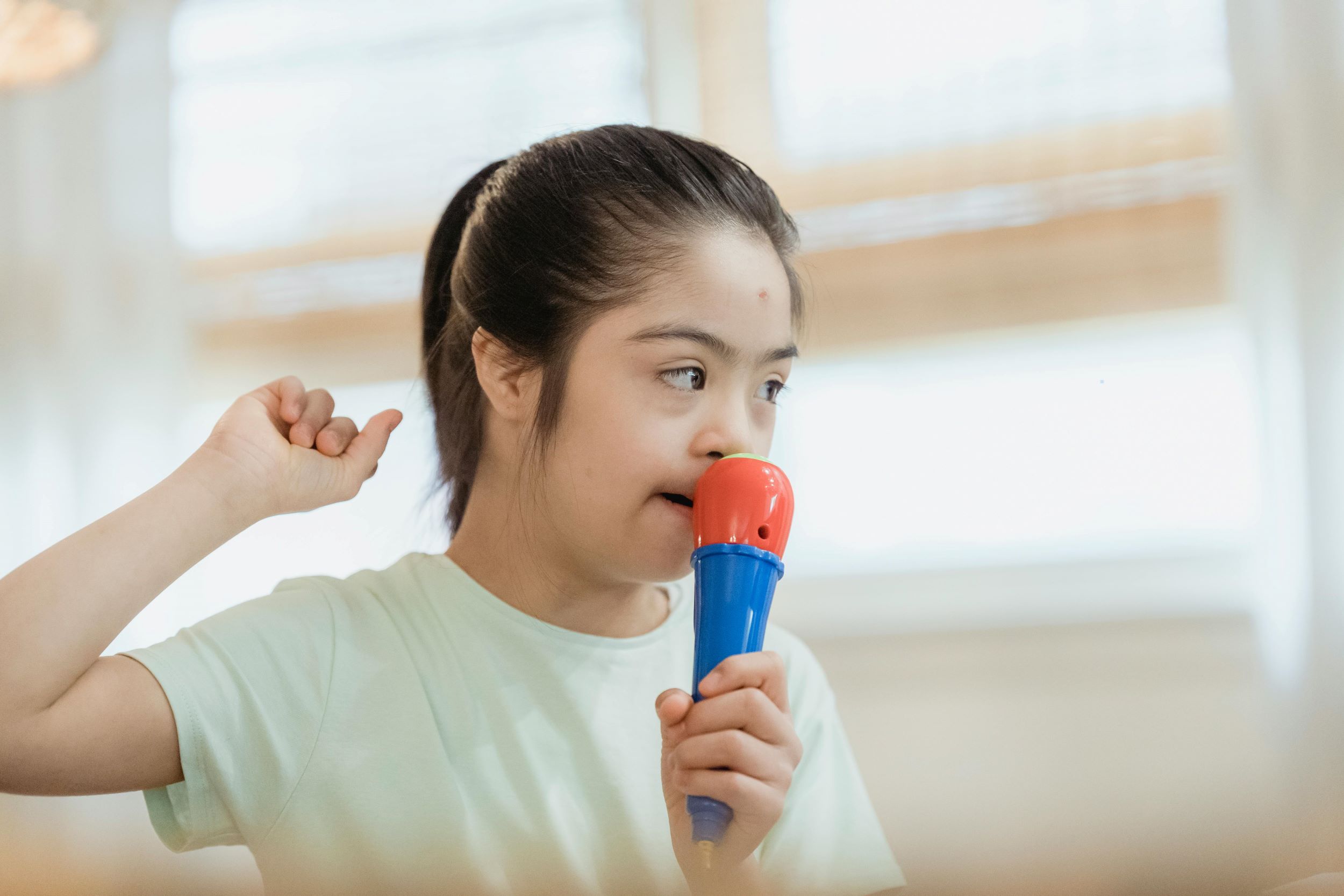 A child with an exceptionality sings while holding a blue and red microphone.
