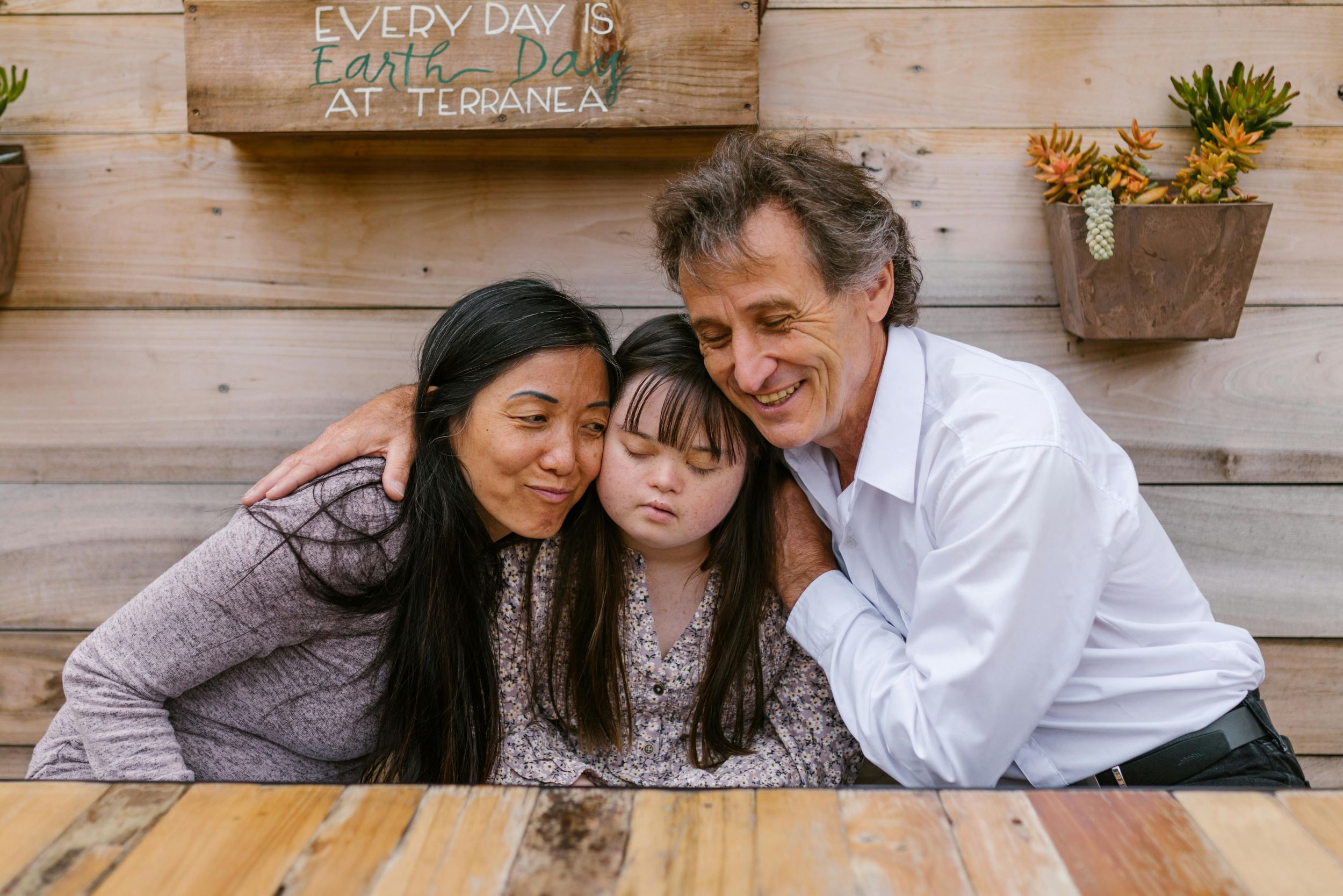 A woman and a man hug a child with exceptionalities.