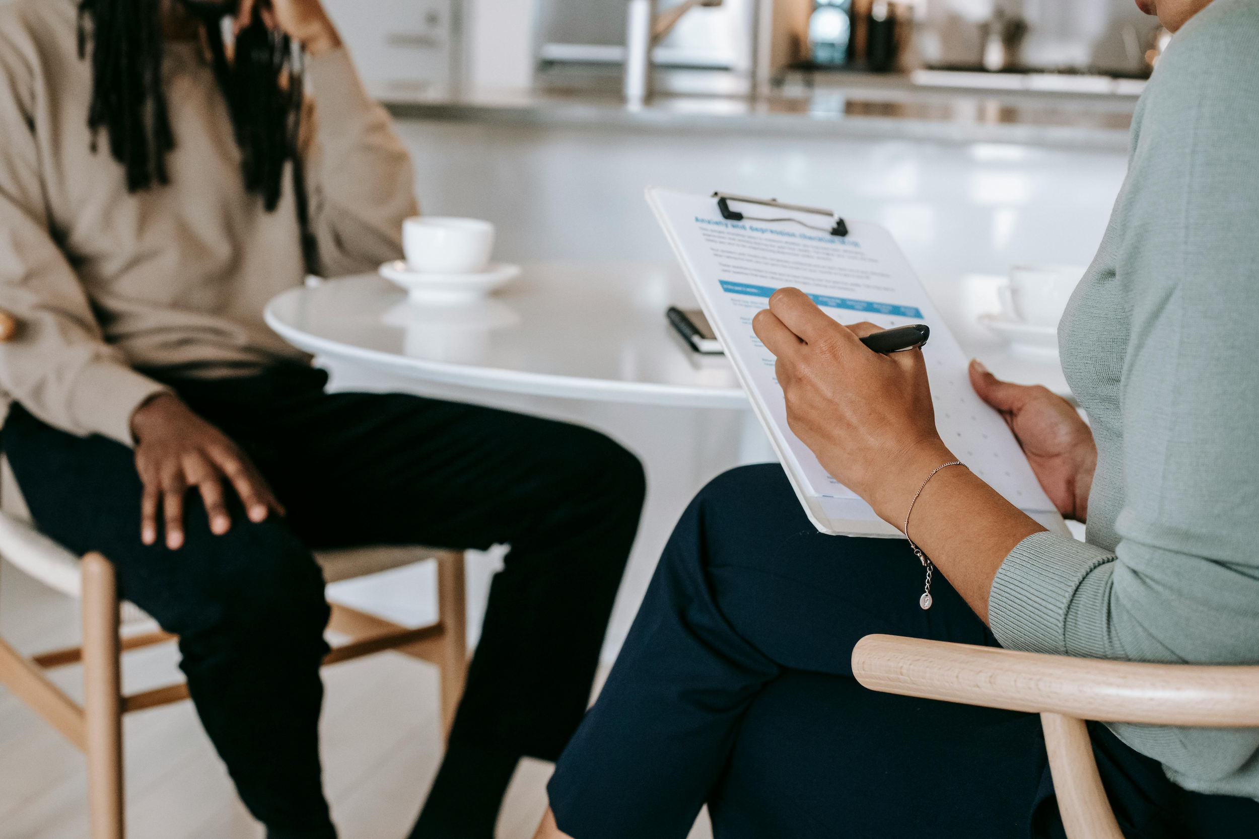 A therapist meets with her client and jots down notes on a paper attached to a clipboard.