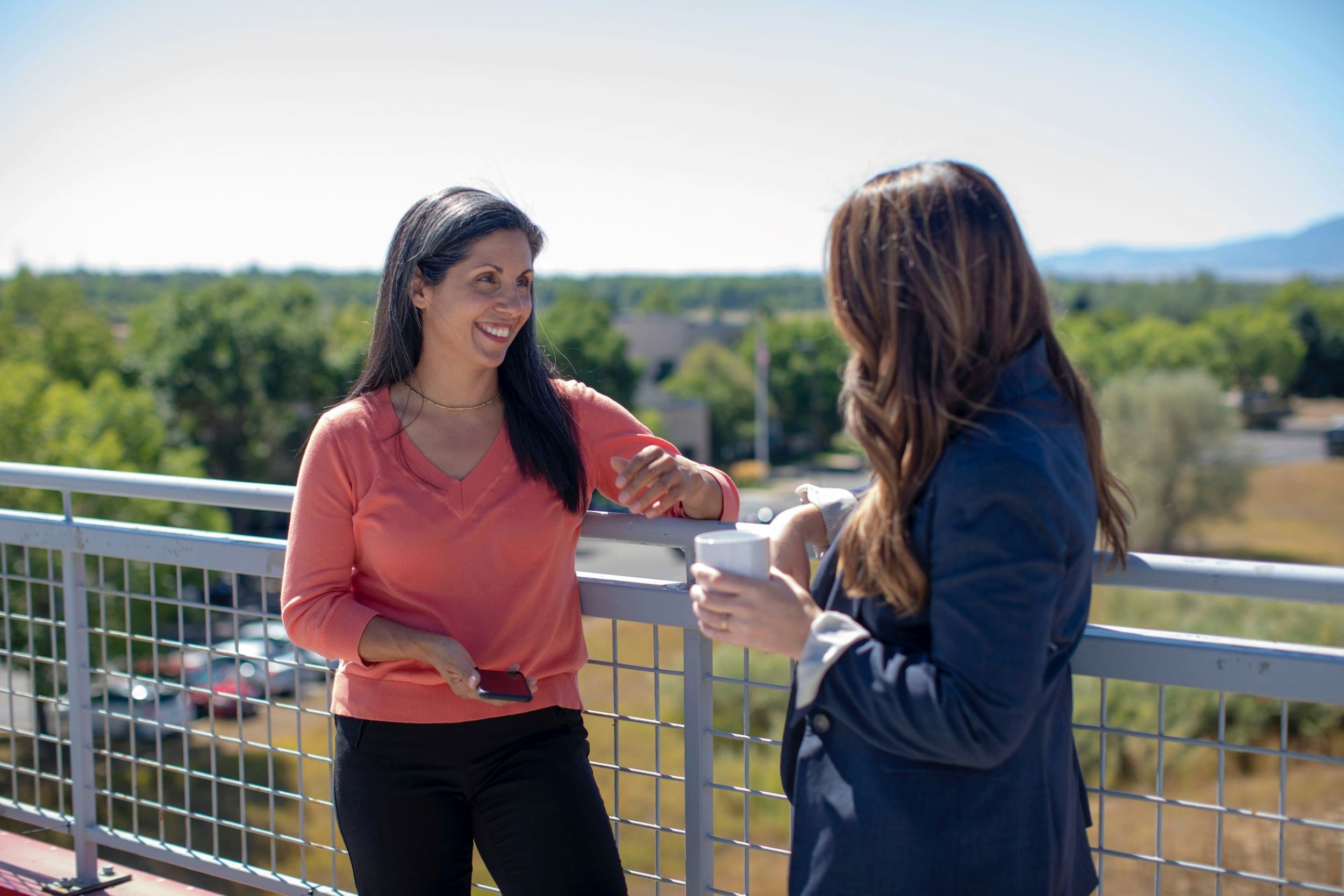 Two women smile while speaking on a bridge.