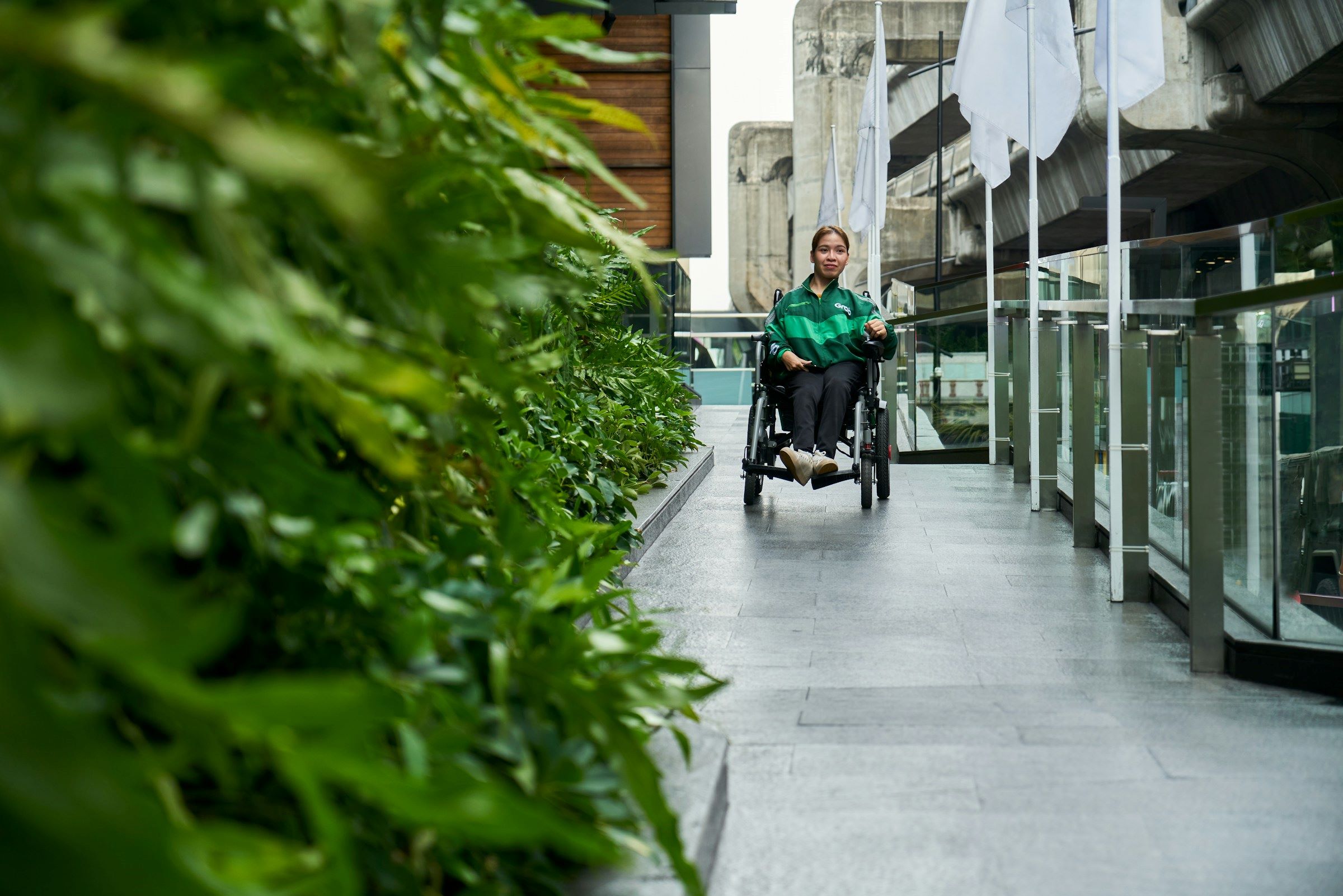 A woman in a wheelchair poses gracefully across from a cluster of bushes.