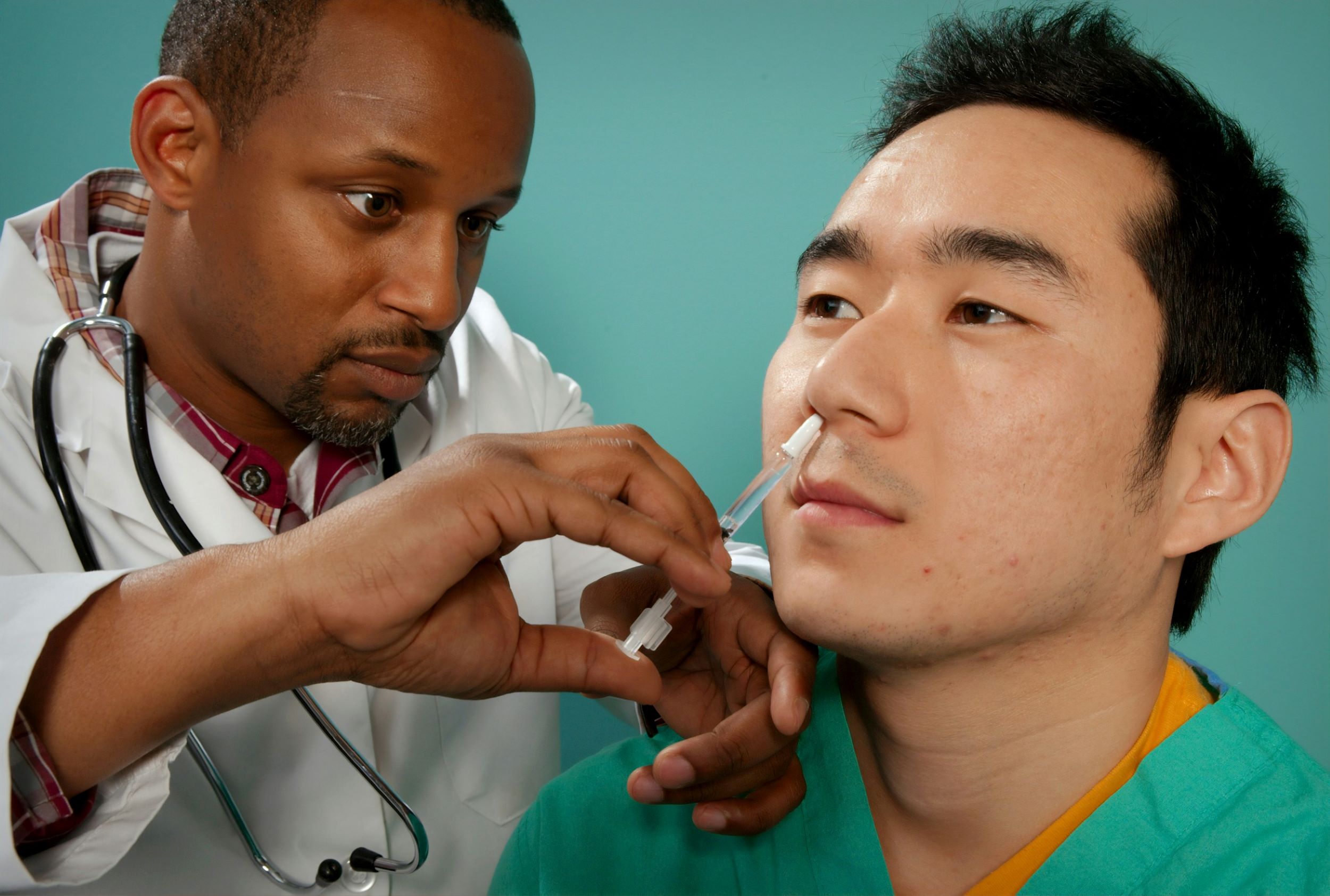 A doctor injects medication into a patient's nose in front of a green backdrop.