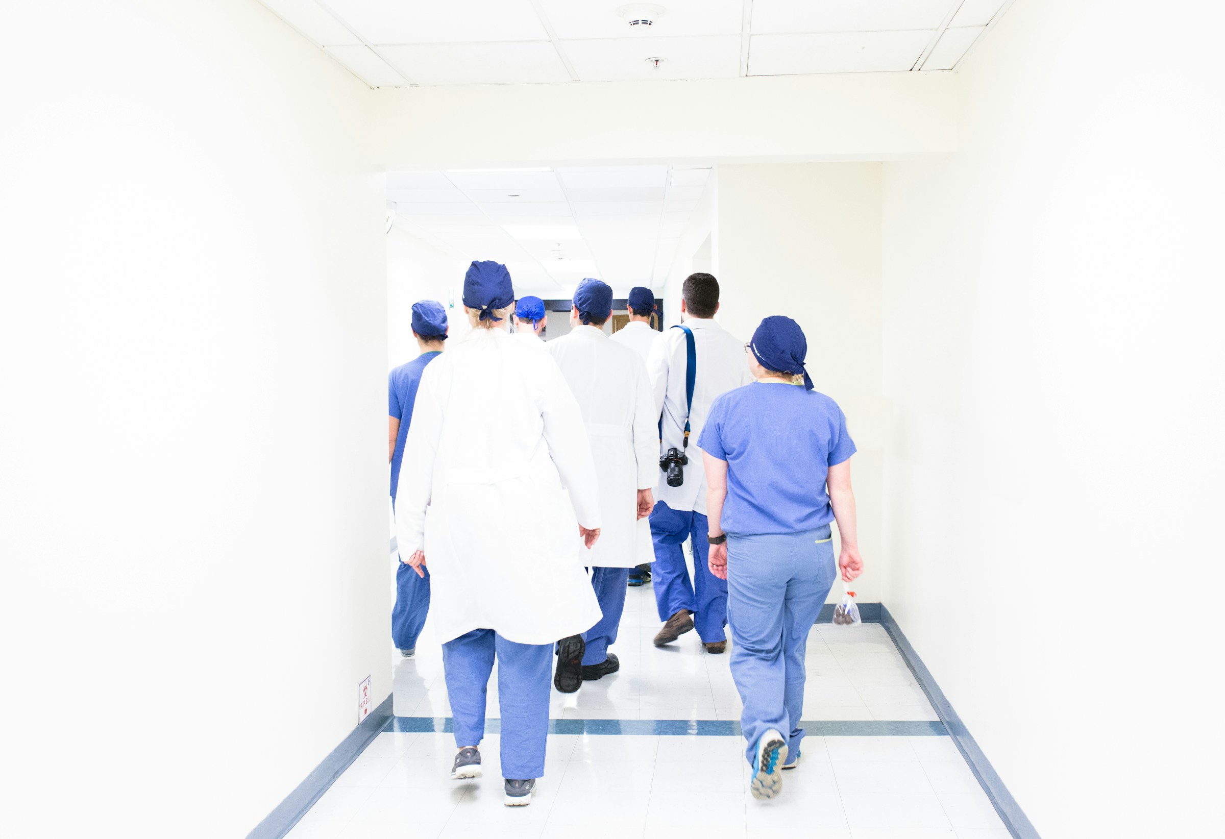Doctors and nurses walk through a spacious hallway with white walls.