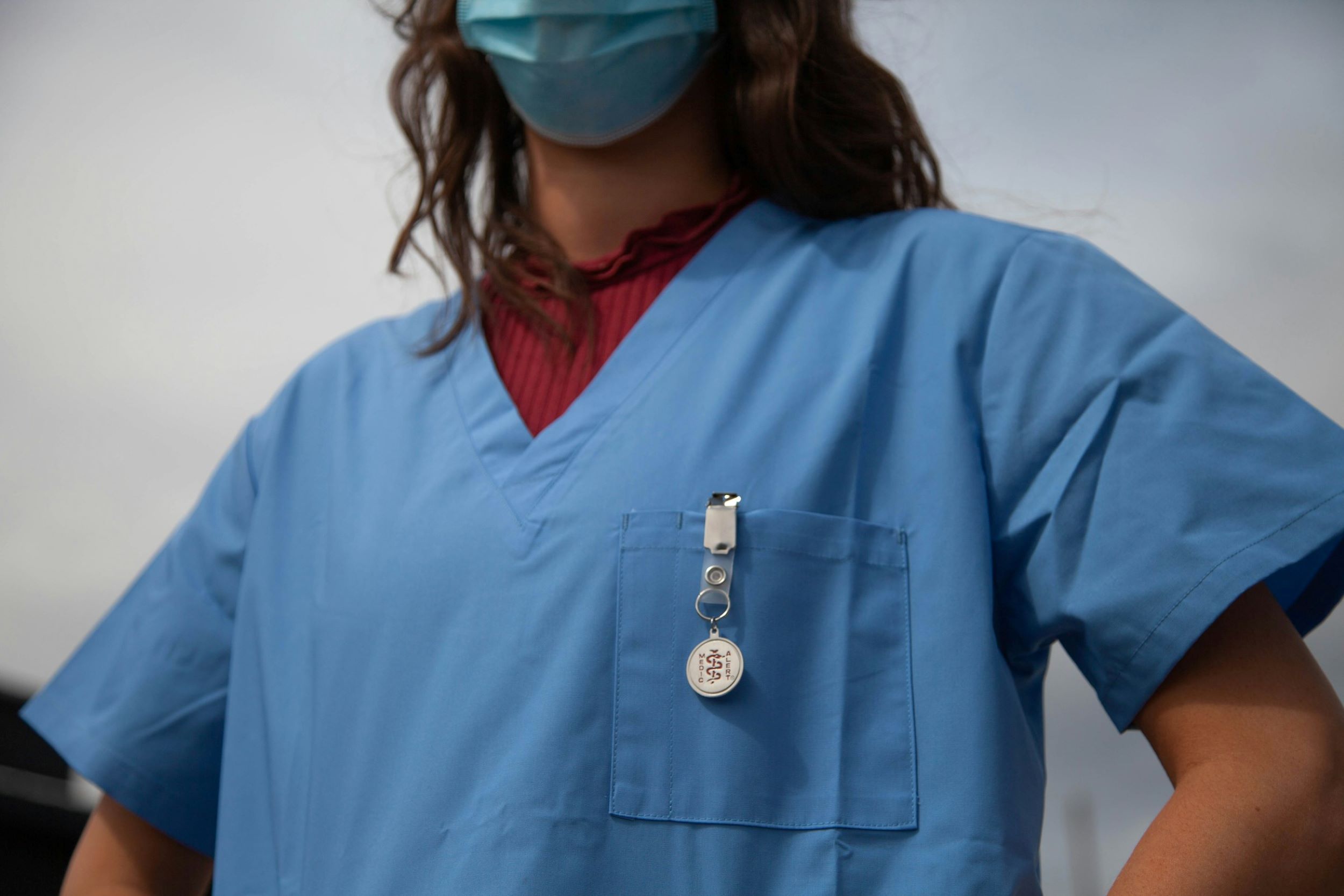 A nurse wears a mask while standing in front of a gray backdrop.