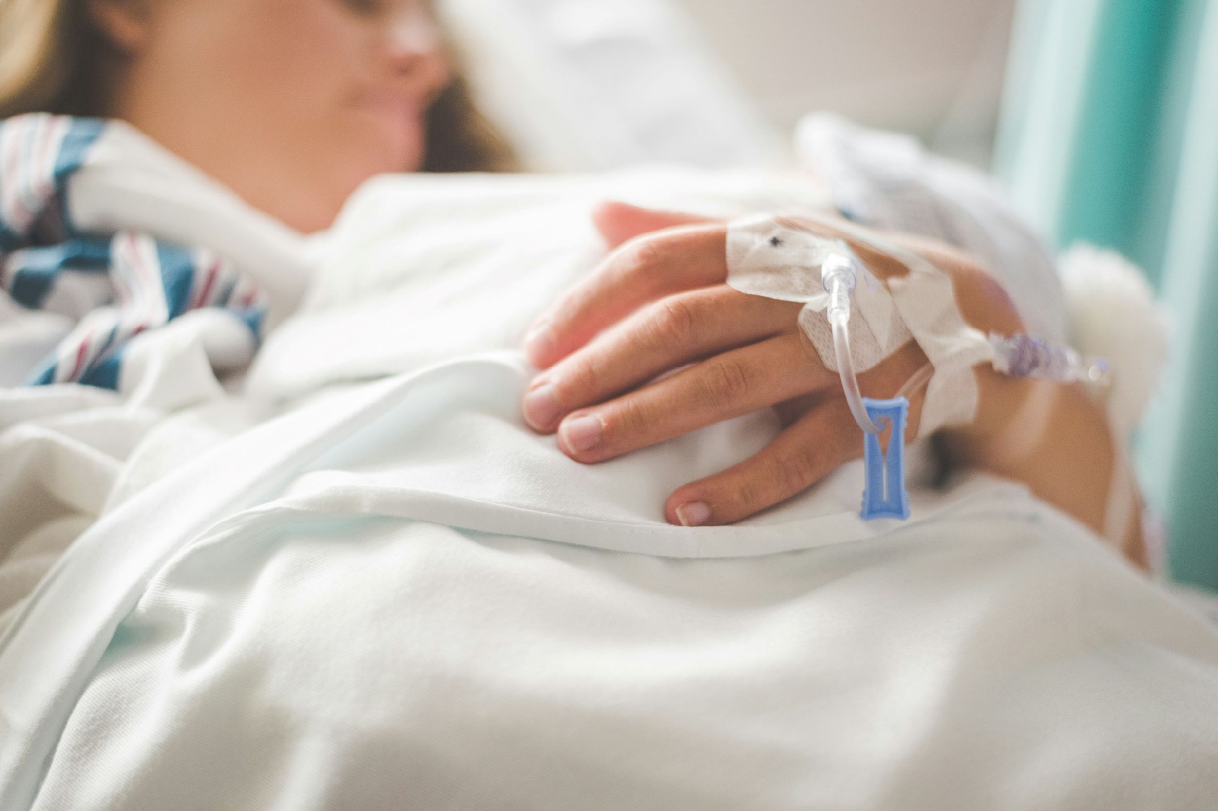 A patient lies in bed, resting her hands on her stomach beneath a soft blanket.