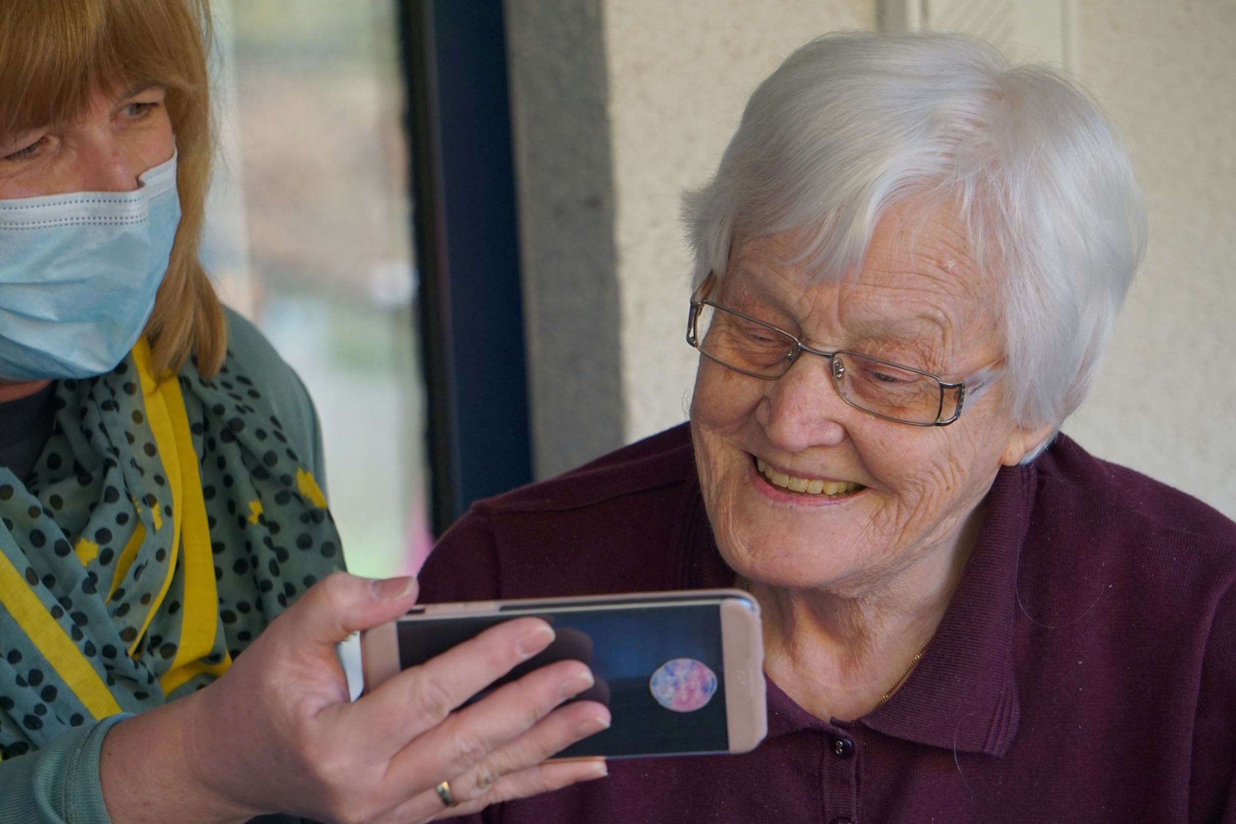 An elderly woman smiles while looking at a cellphone.