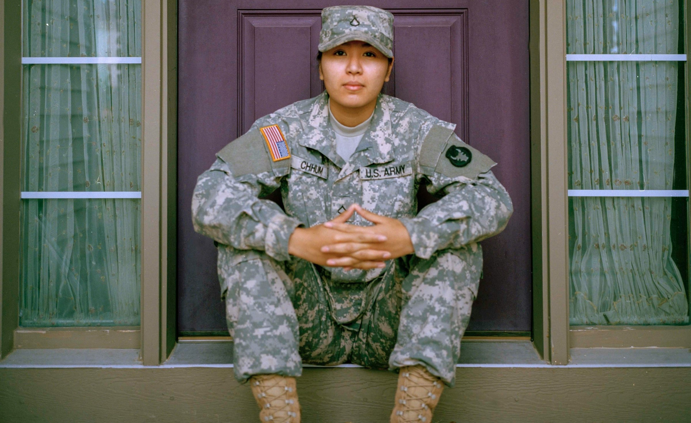 A soldier sits near the doorway of the house.