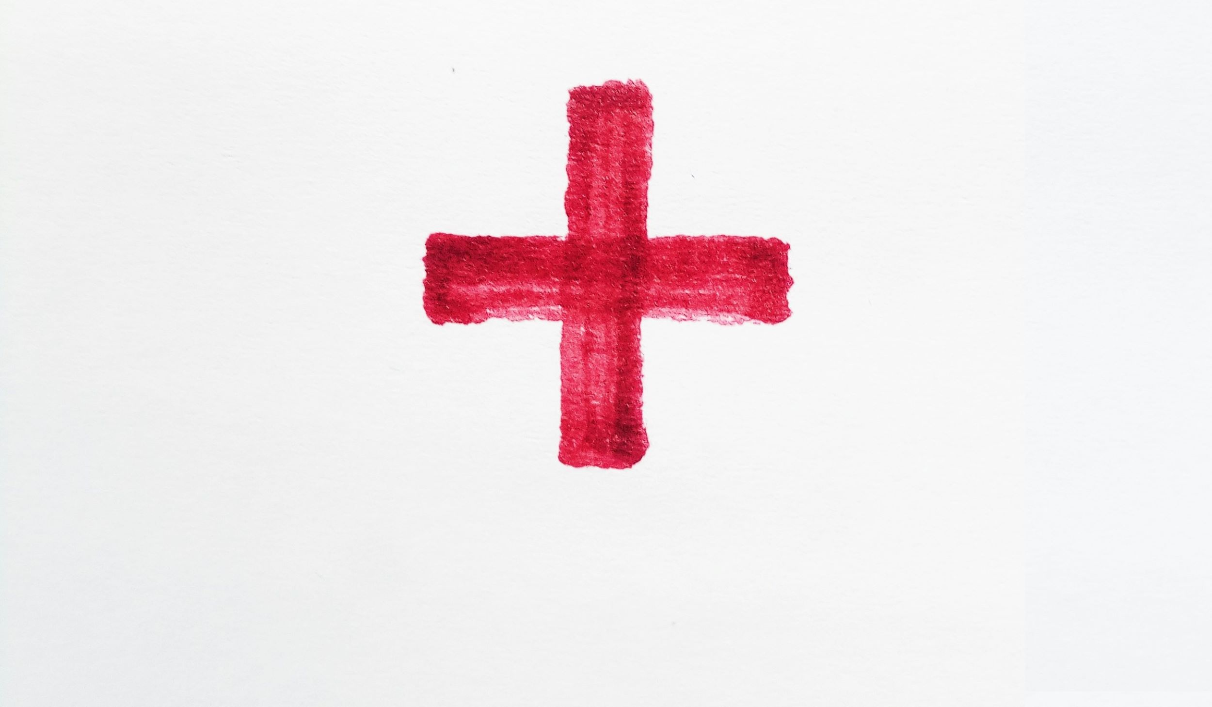 A bright red cross is positioned in front of a white backdrop.