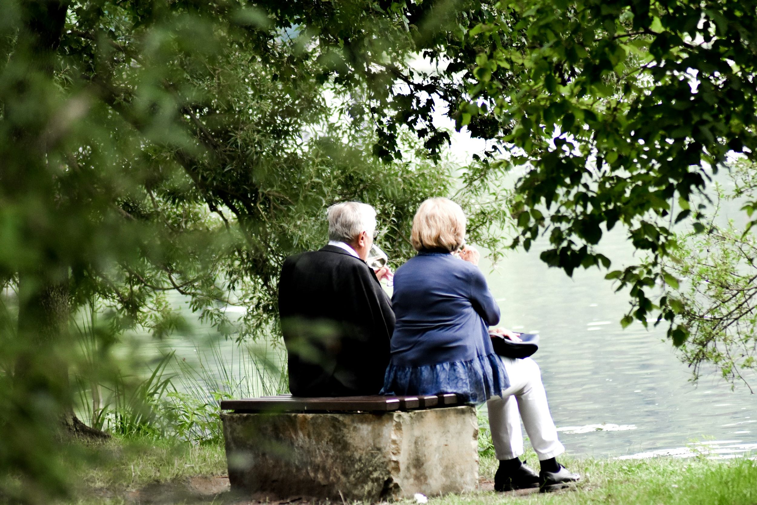 Two elderly individuals enjoy wine and watch the movement of the sea.