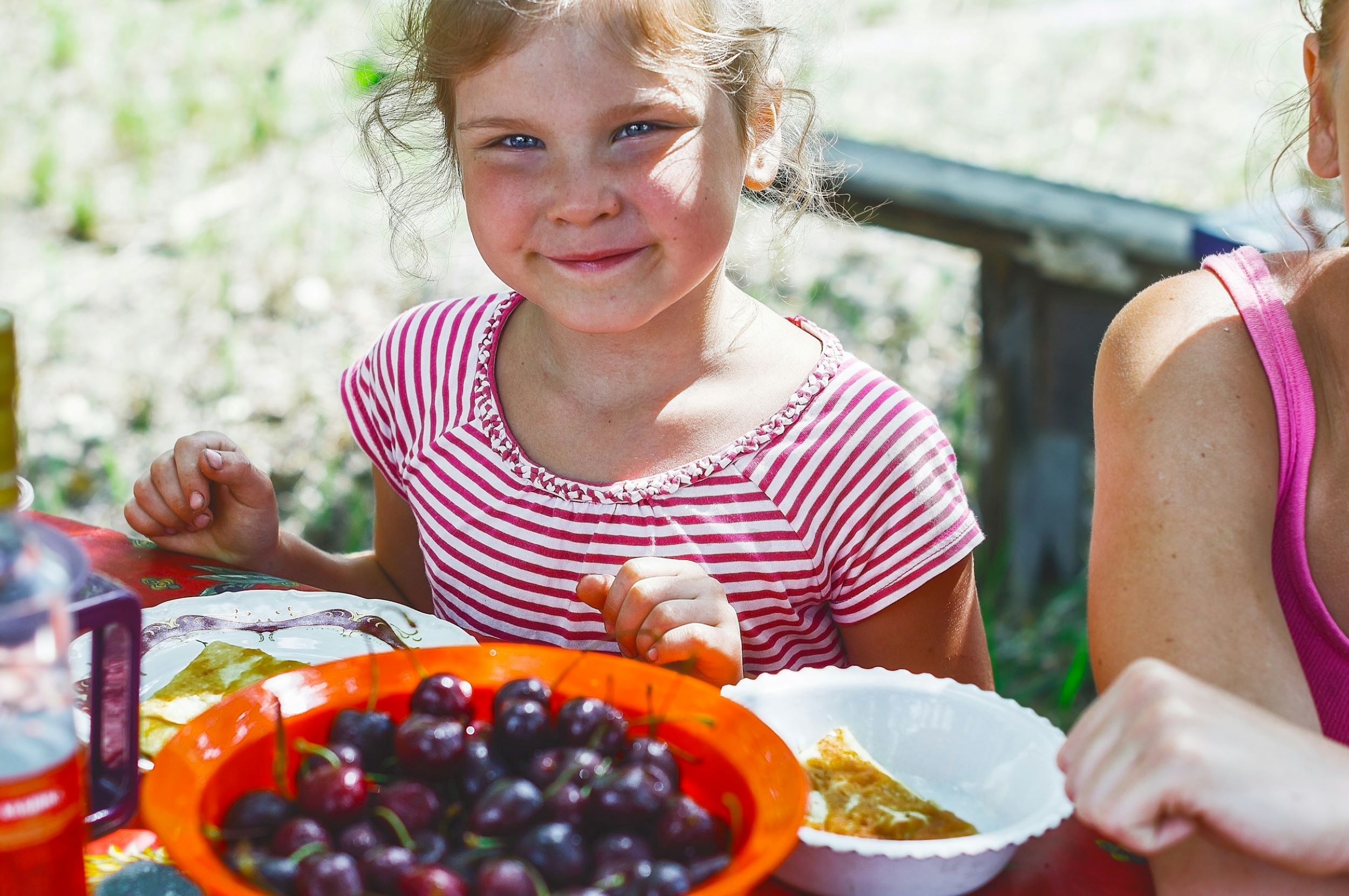 A smiling girl sits at a table with berries in front of her.