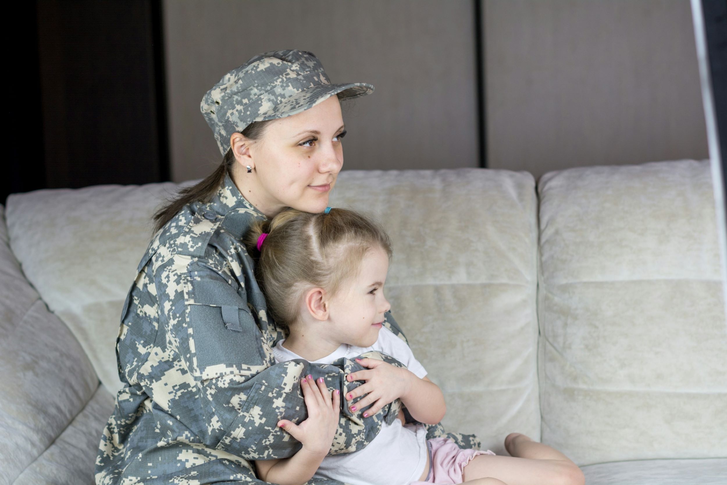 A soldier sits on a couch and hugs her daughter.