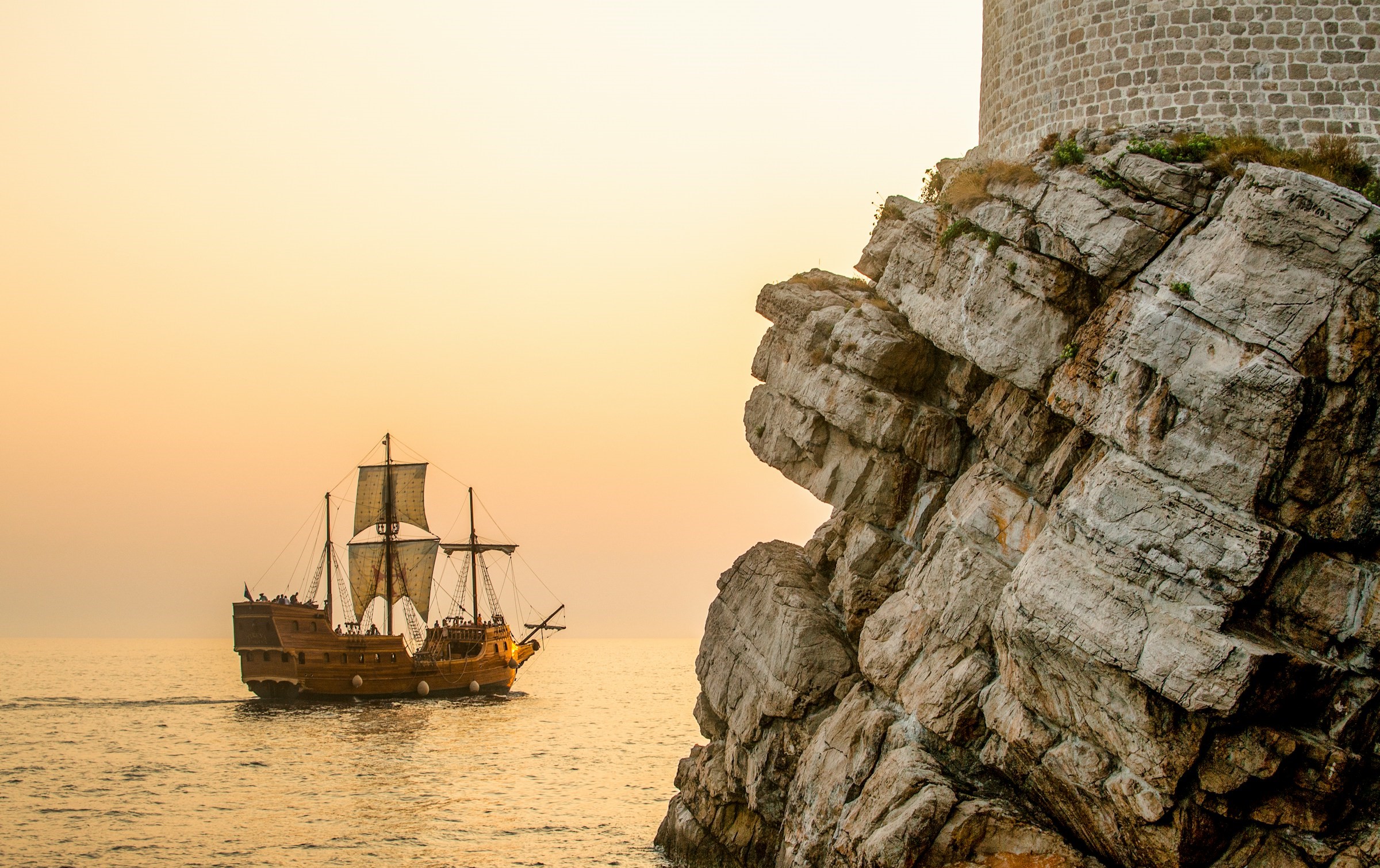 A pirate ship sails slowly past a lighthouse.