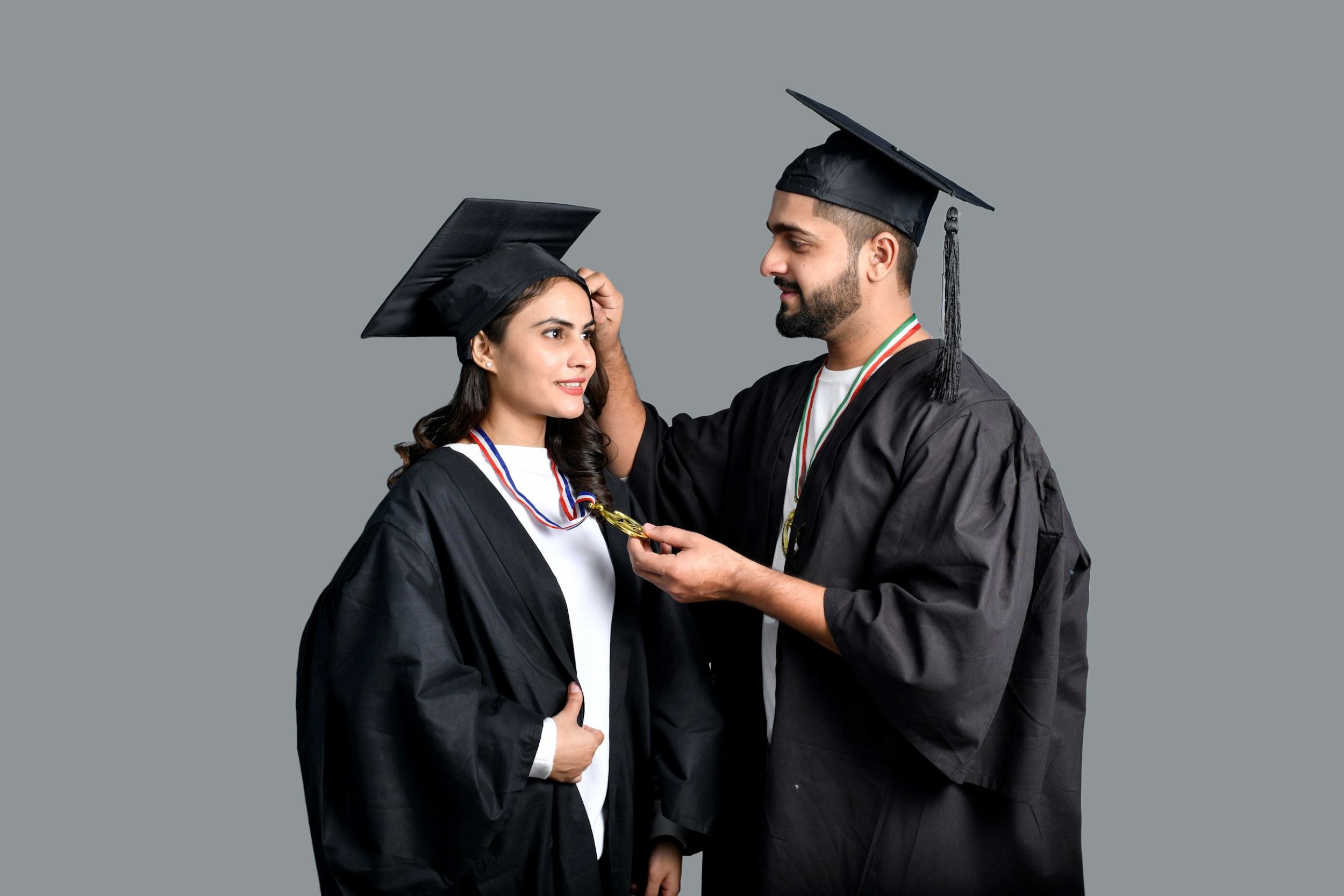 A mentor and a graduate, both dressed in caps and gowns, share a warm smile with each other.