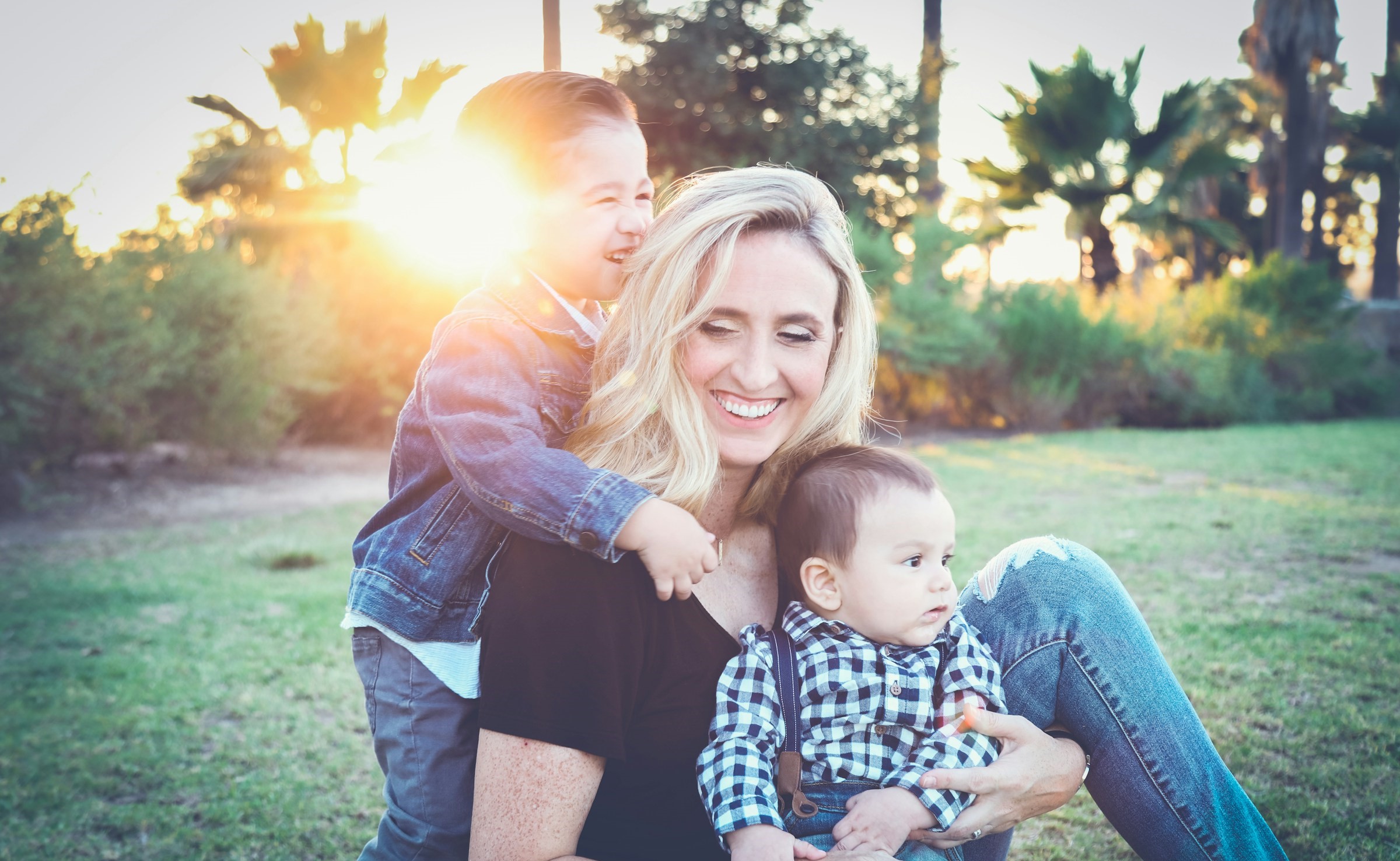 A mother sits on the grass, smiling as she enjoys the moment with her children.