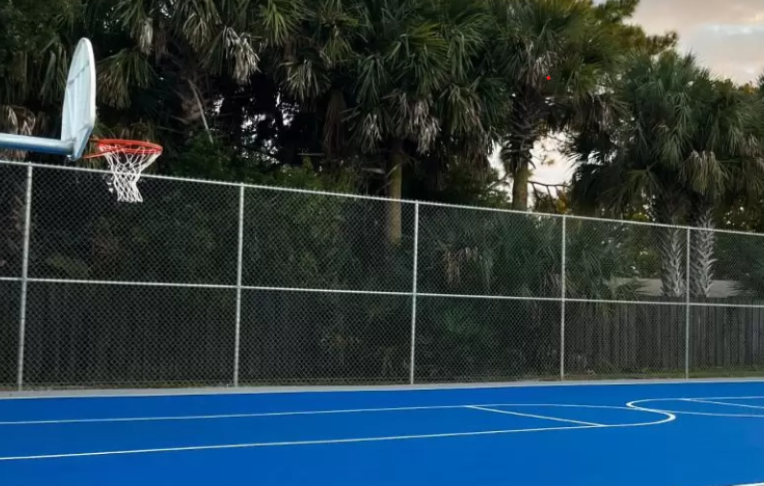 A basketball court sits quiet and deserted as the sun sets, casting a warm glow over the empty pavement.