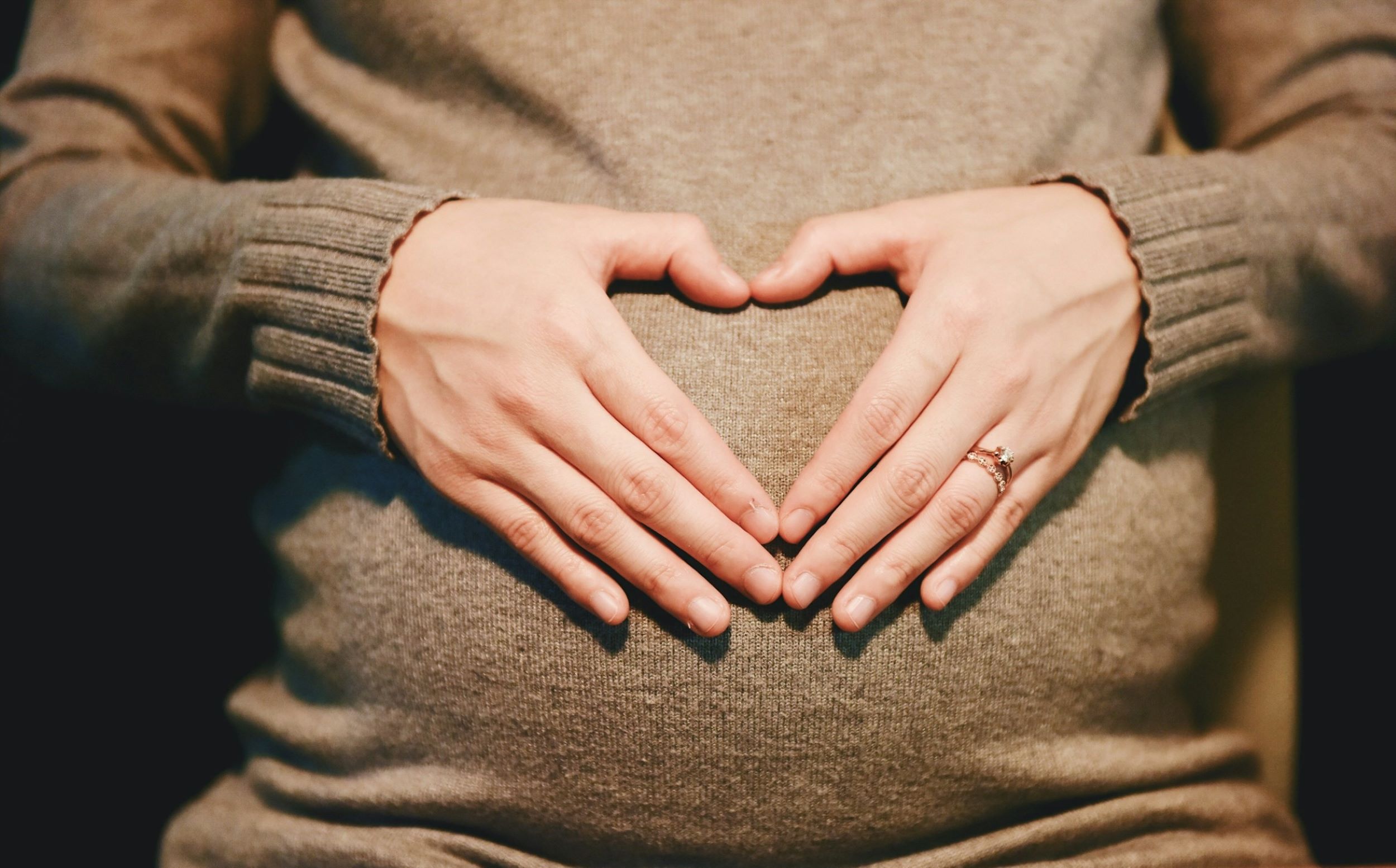 A pregnant woman gently shapes her hands into a heart over her belly.