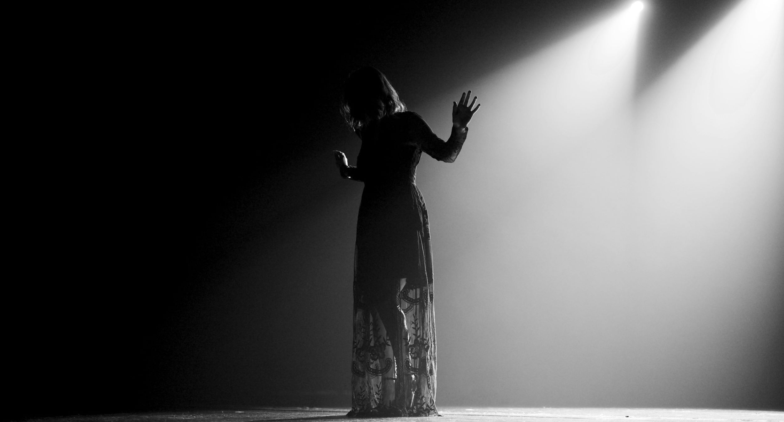 A woman stands on the stage with her hands raised to the side of her body.