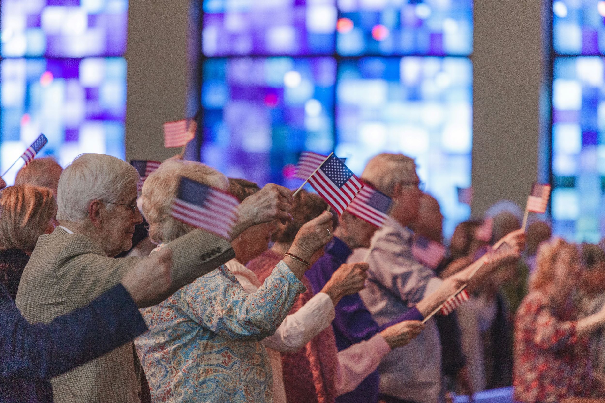Senior men and women wave small American flags within a church. 