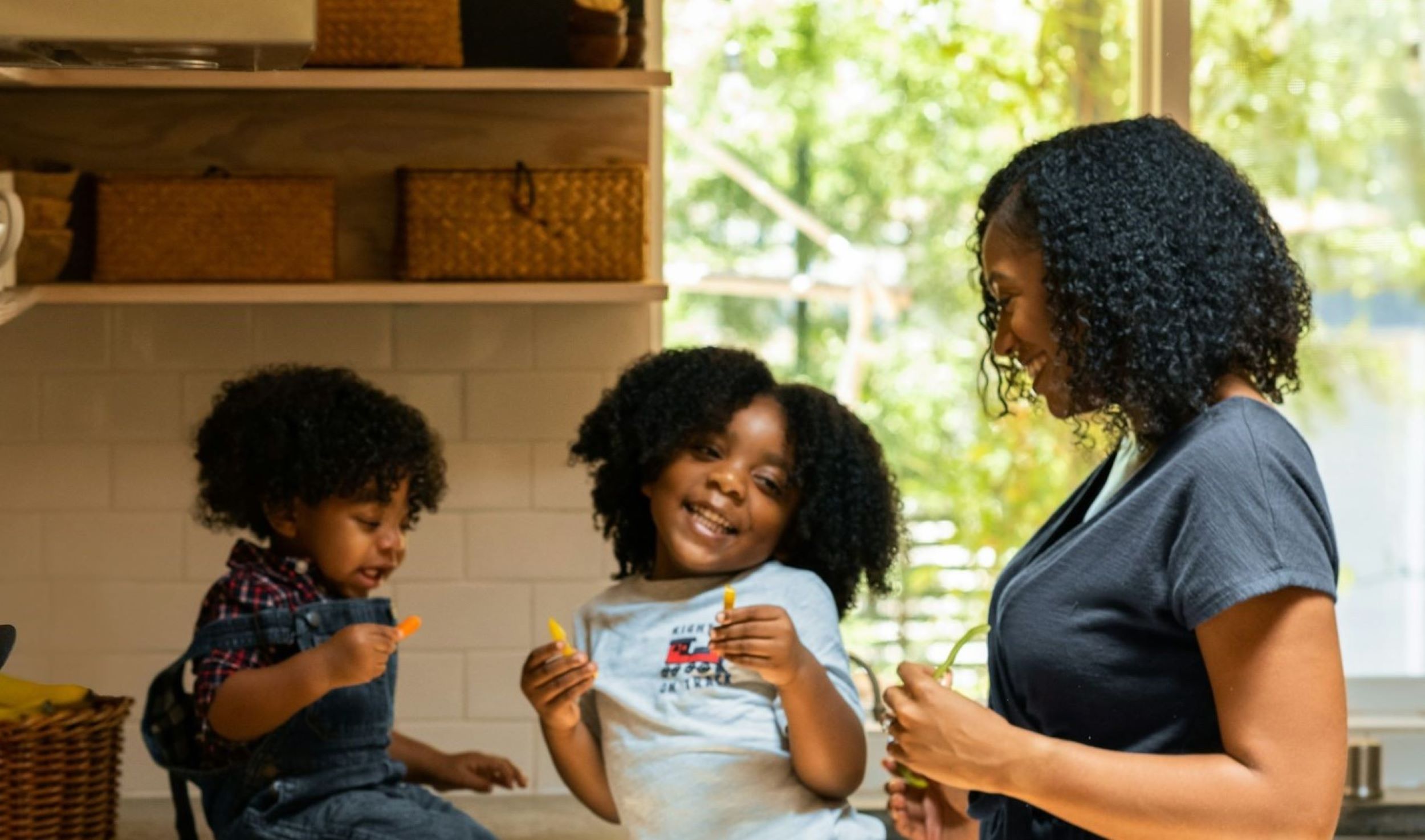 A family smiles while gathering in the kitchen.
