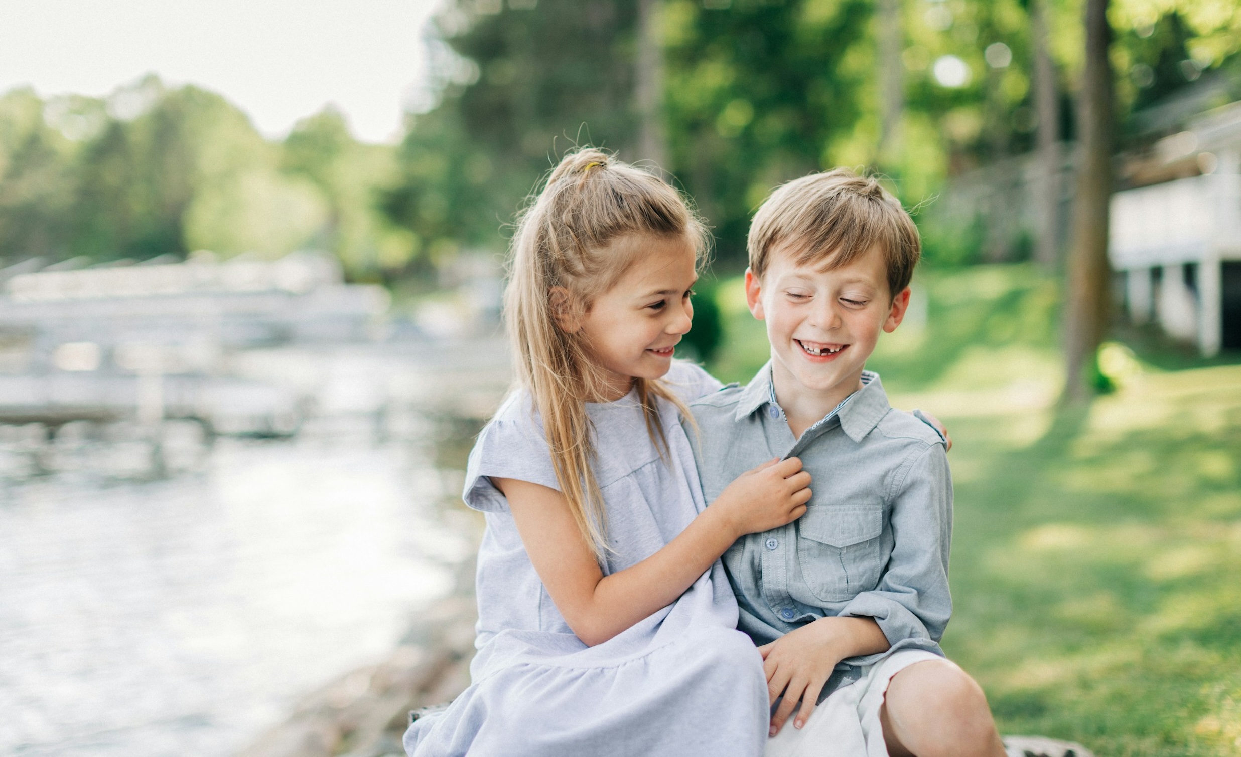 Smiling children sit peacefully by a lake surrounded by open grassland.