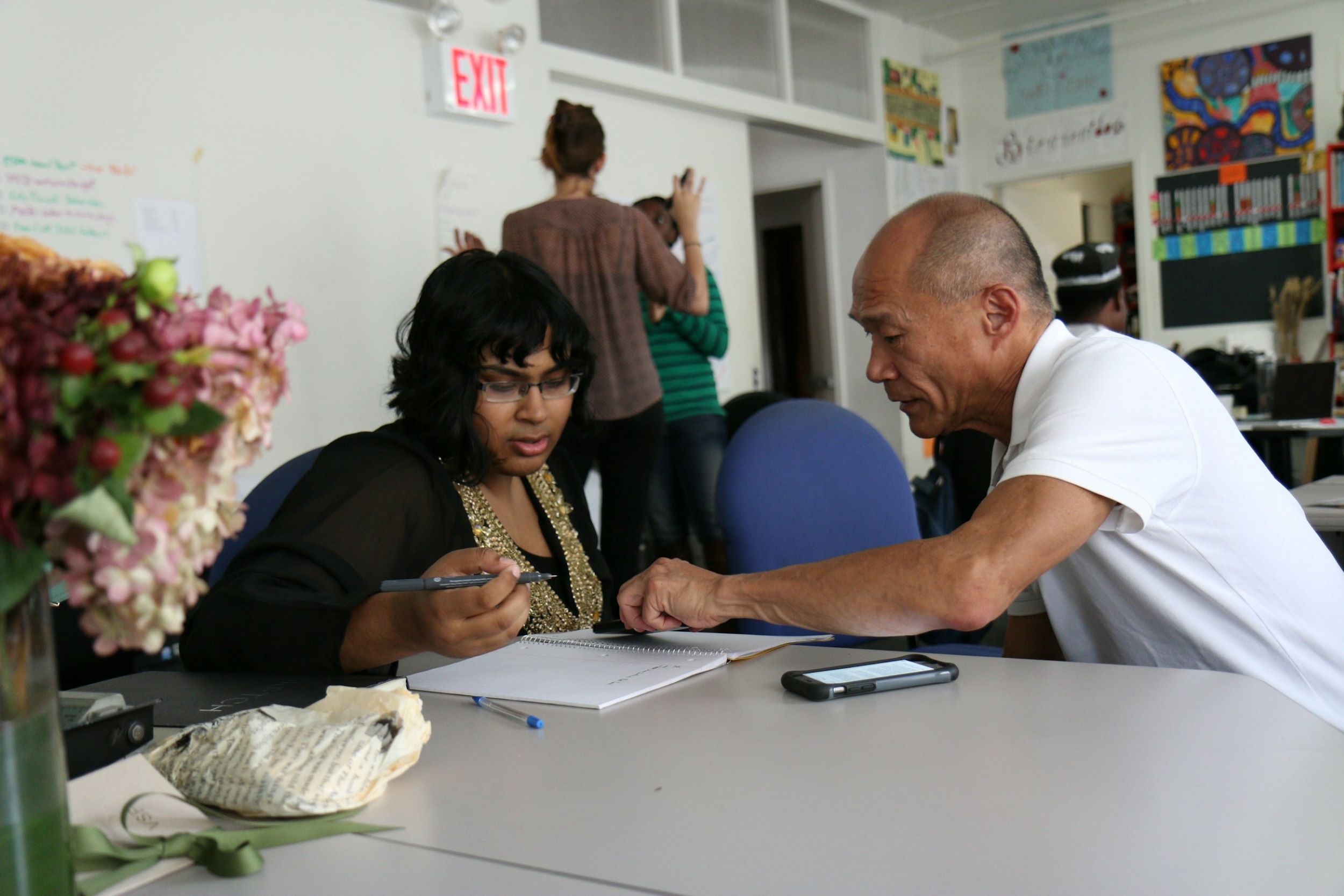 A counselor speaks with a woman in his office, while pointing to a notebook.