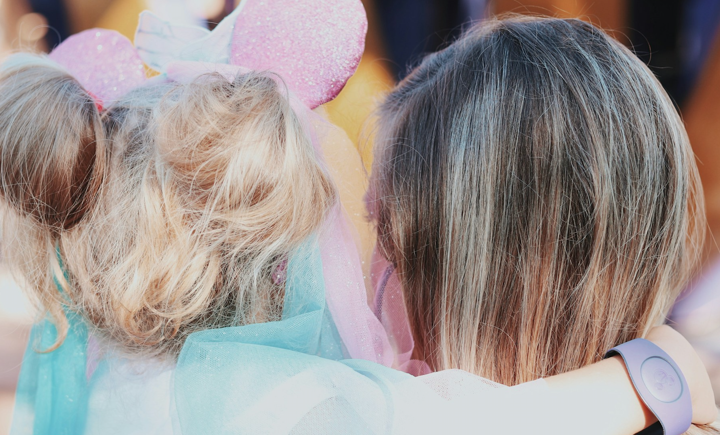 A young girl wears Minnie Mouse ears while being held lovingly by her mother.