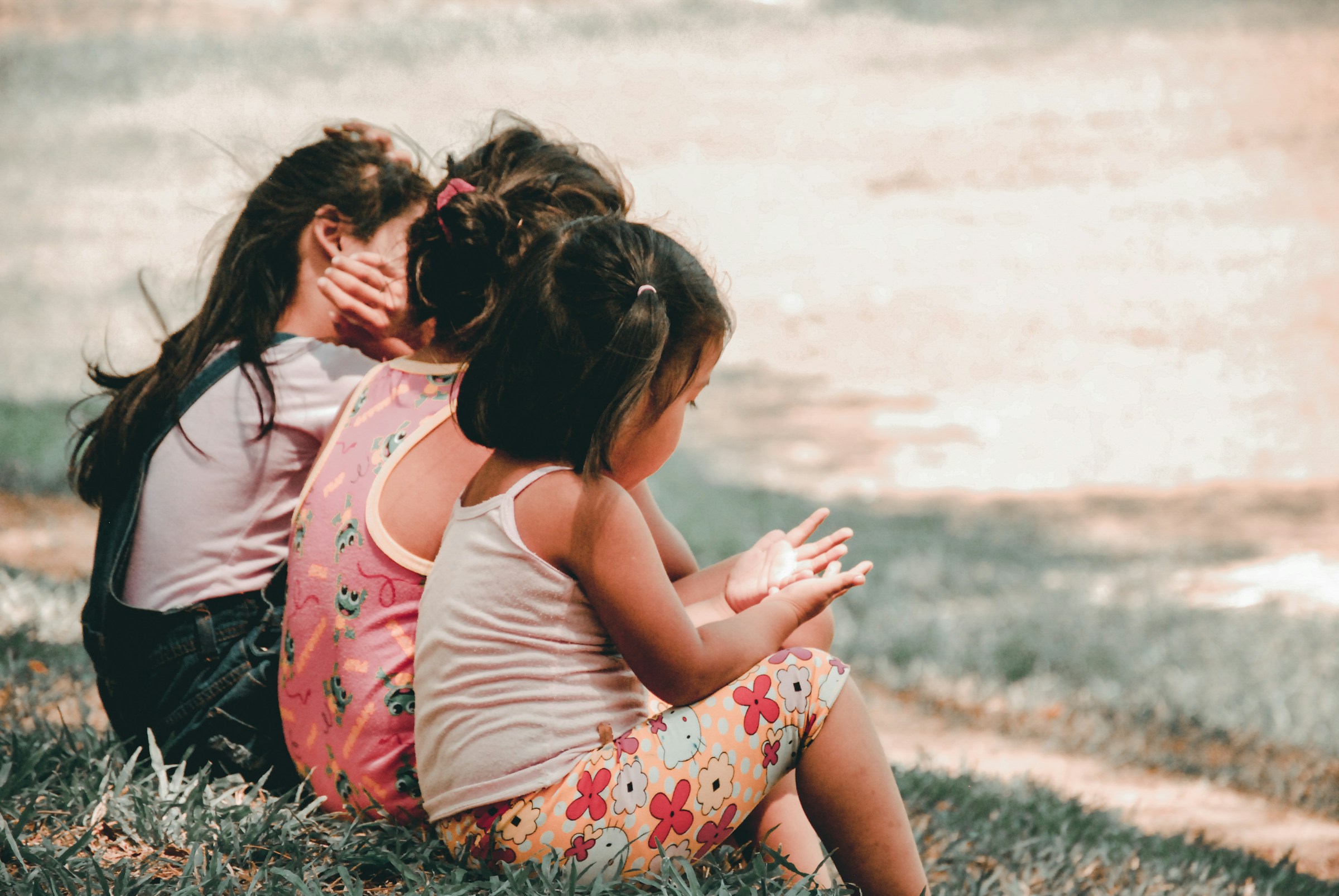 Three young girls sit on a small hill.