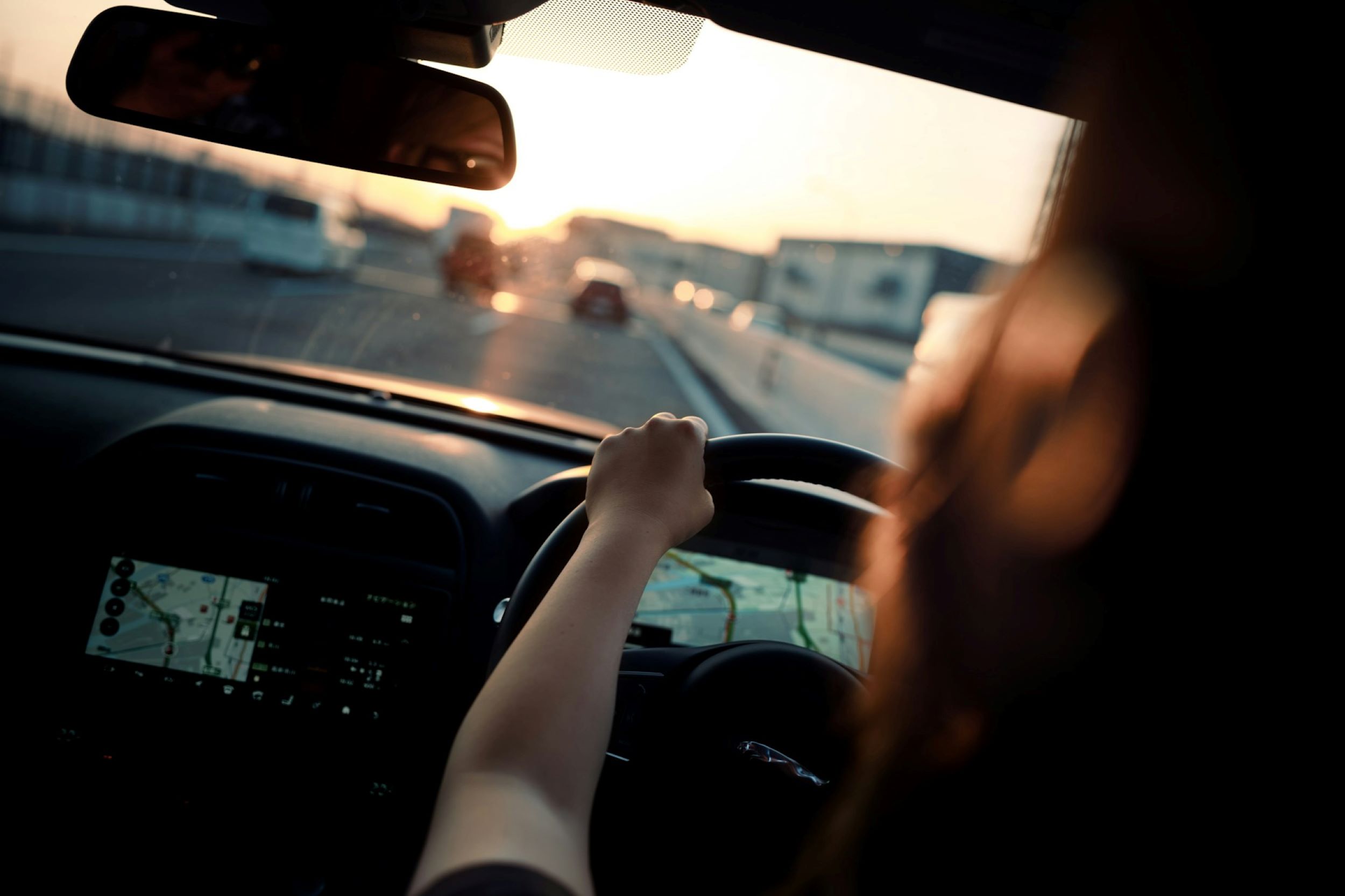A woman drives along the highway as the sun sets on the horizon.
